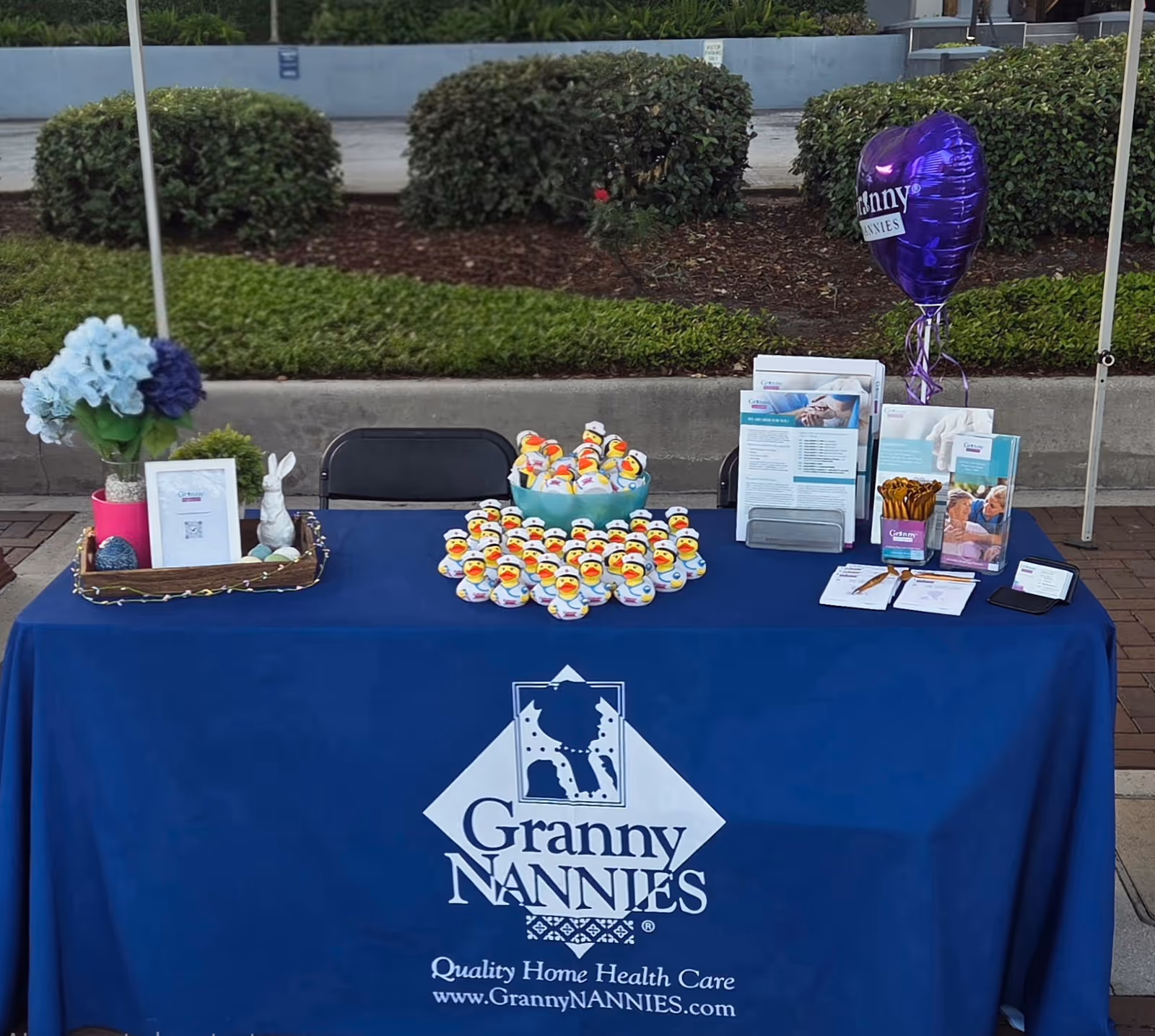 Outdoor promotional table featuring Granny Nannies banner, brochures, and a bowl of rubber ducks.