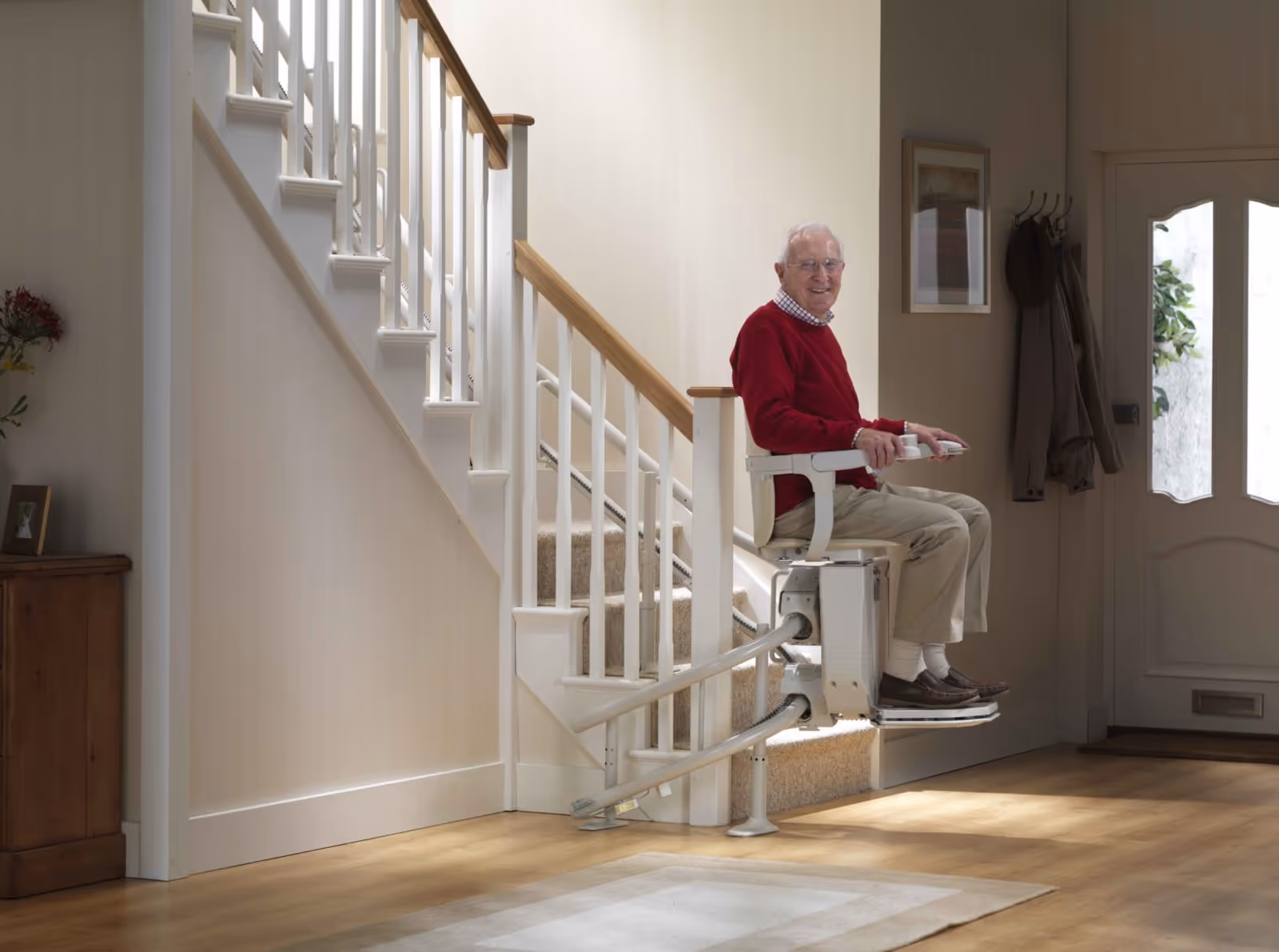 Elderly man seated on a stairlift beside a staircase in a senior living facility.
