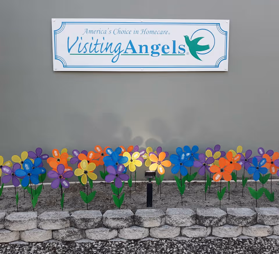 Exterior wall with Visiting Angels sign and colorful pinwheels along a stone border