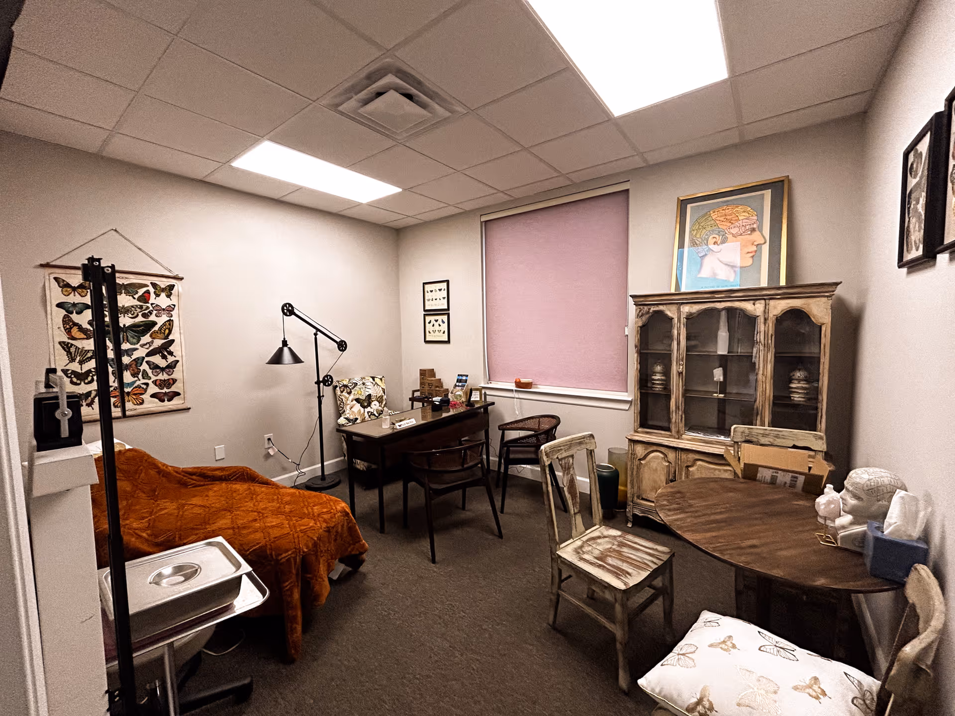 A small furnished room with a bed, desk, cabinet, and round table.