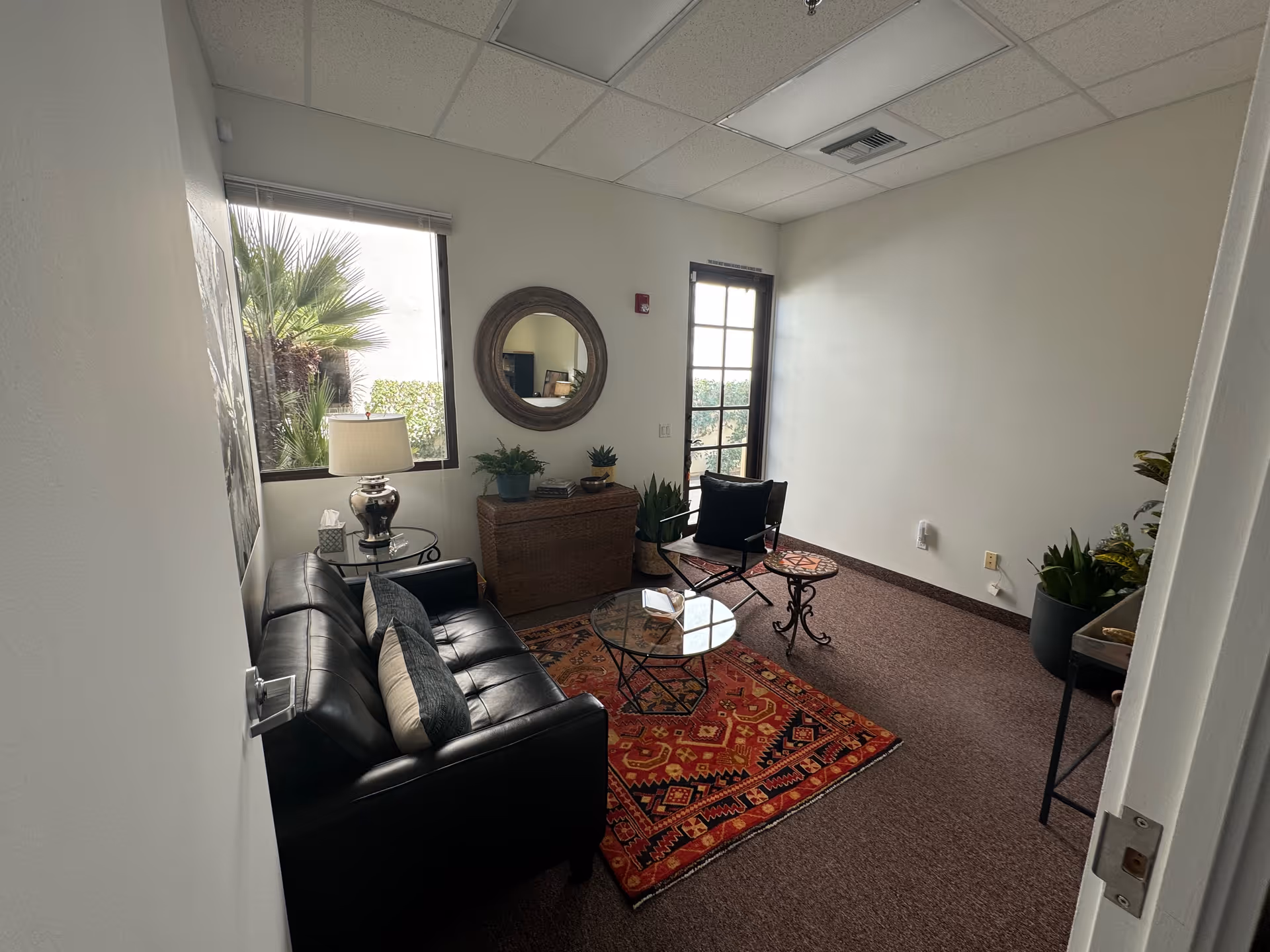 Small lounge in a senior living facility with black leather sofa, glass tables, rug, and plants.