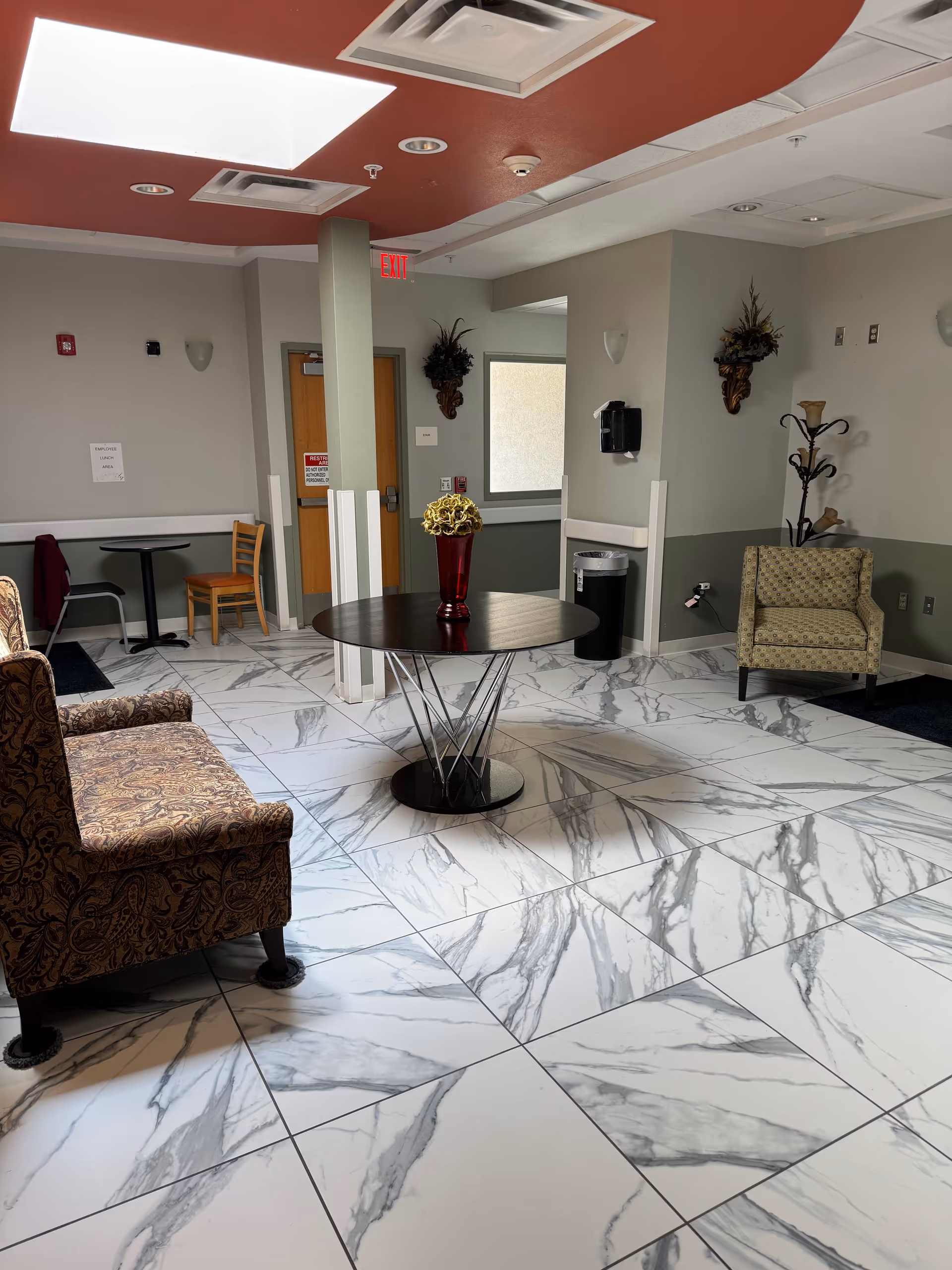 Bright lobby with marble floors, round table, chairs, and decorative wall accents.