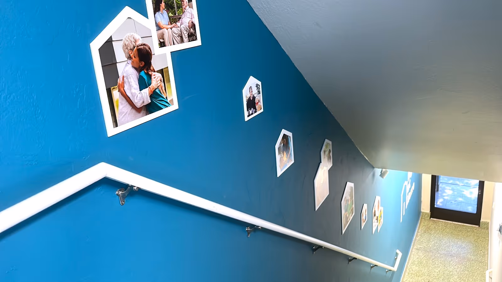 Blue hallway with photo frames mounted along a staircase and a white handrail.
