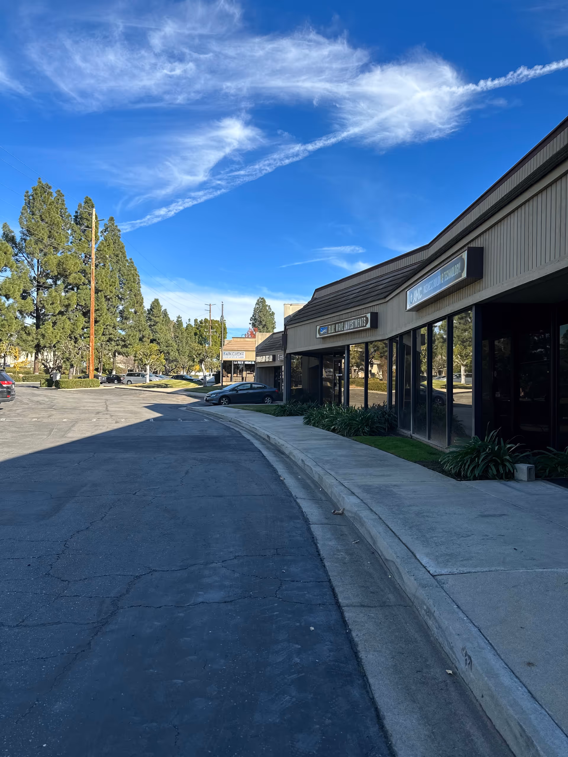 Exterior view of a senior facility with storefronts, a curved driveway, and blue sky.