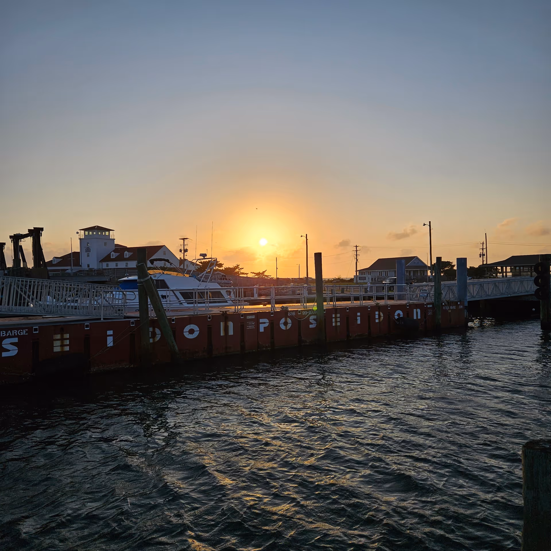 Sunset over a harbor with boats docked along a pier and calm water.