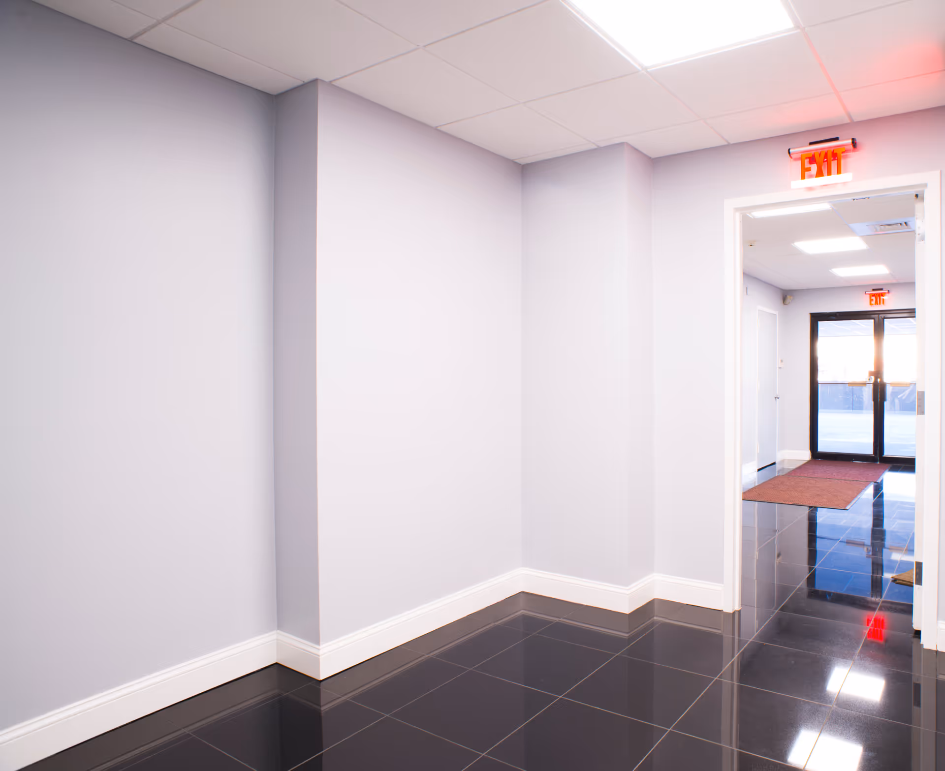 Light purple hallway with glossy black tile floor and an exit doorway.