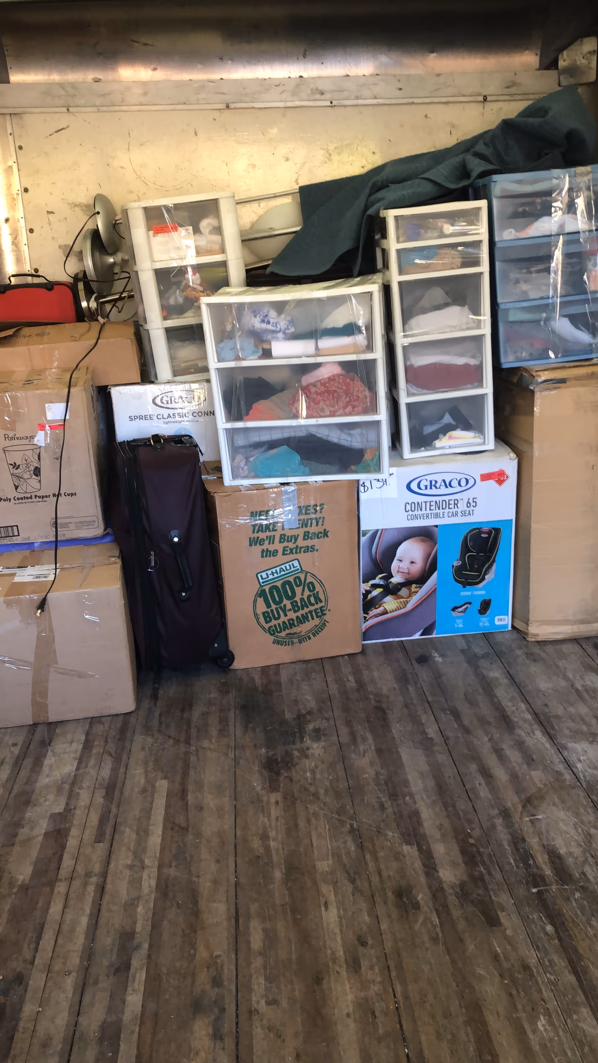 A cluttered storage room with plastic drawers, packed boxes, and exposed wooden floor.