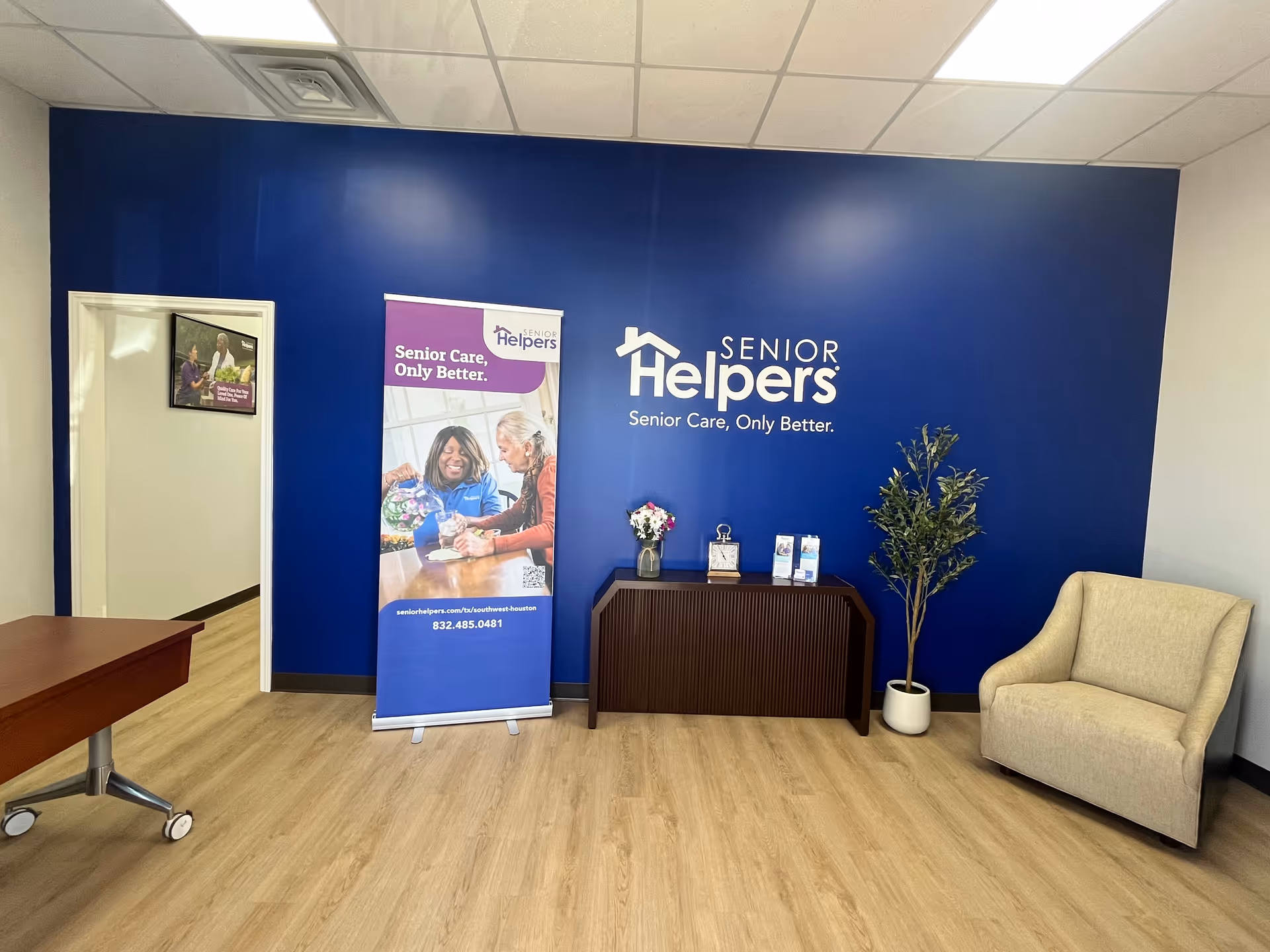 Reception lobby with blue wall, Senior Helpers branding, banners, desk, and beige armchair.
