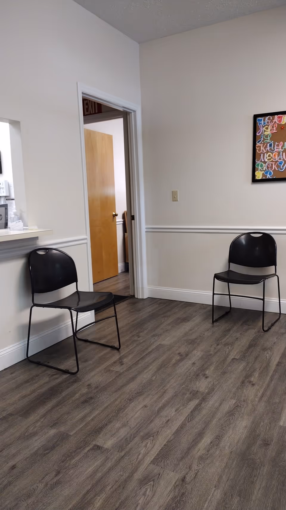 Two black chairs sit in a quiet room with vinyl plank flooring near an exit doorway.