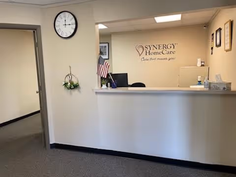 Reception desk in a facility lobby with an American flag and Synergy HomeCare sign.