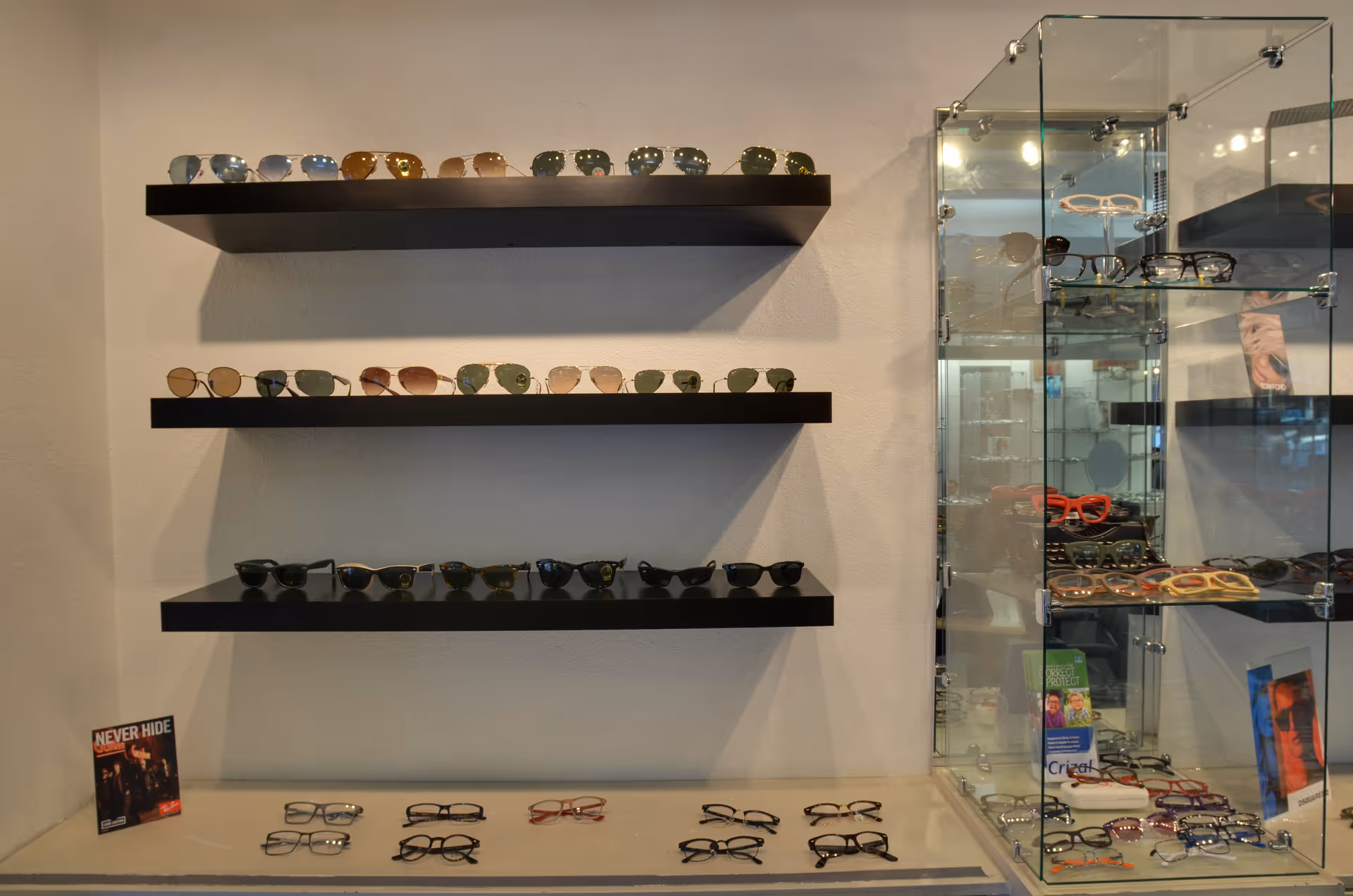 A display of sunglasses on wall shelves beside a glass retail cabinet