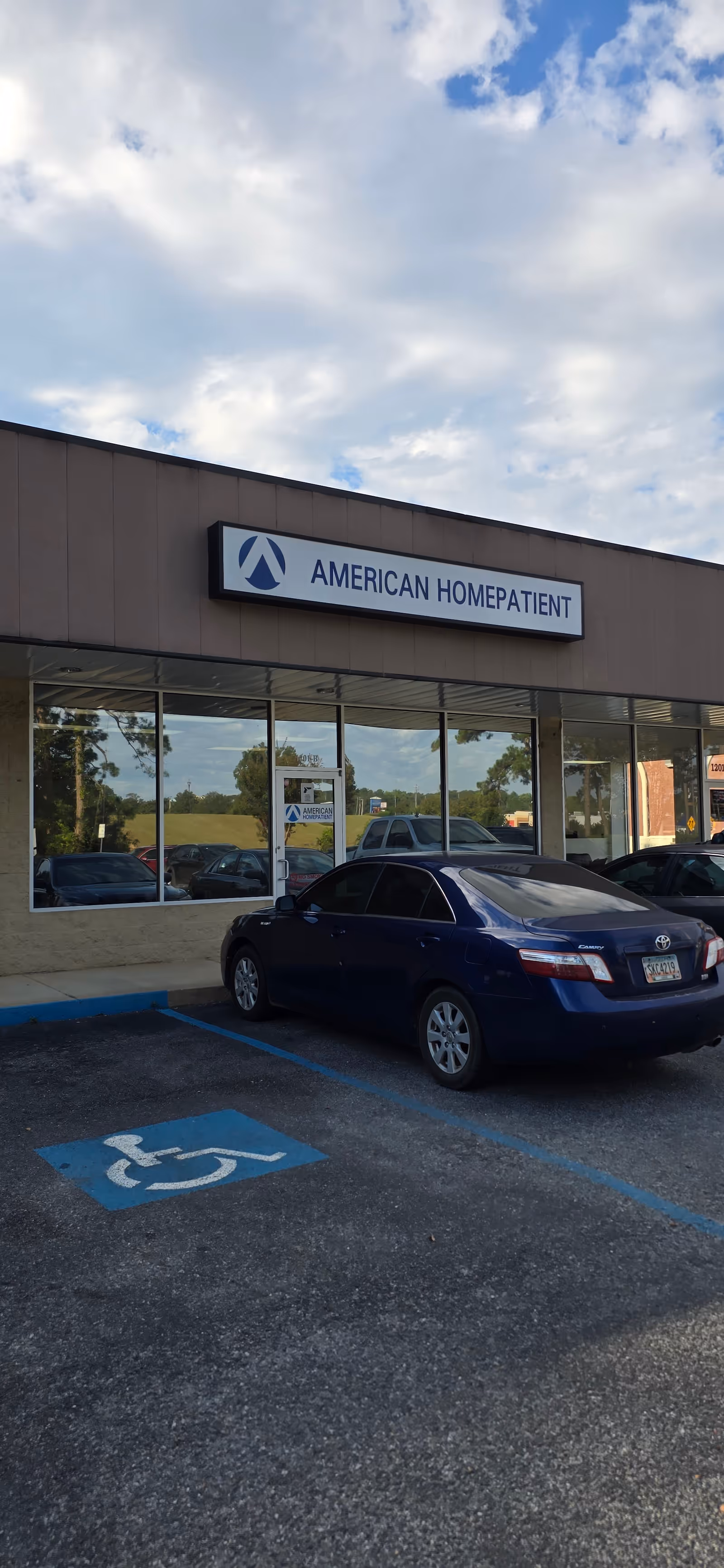 Exterior view of a facility with a sign reading American HomePatient and parked cars.