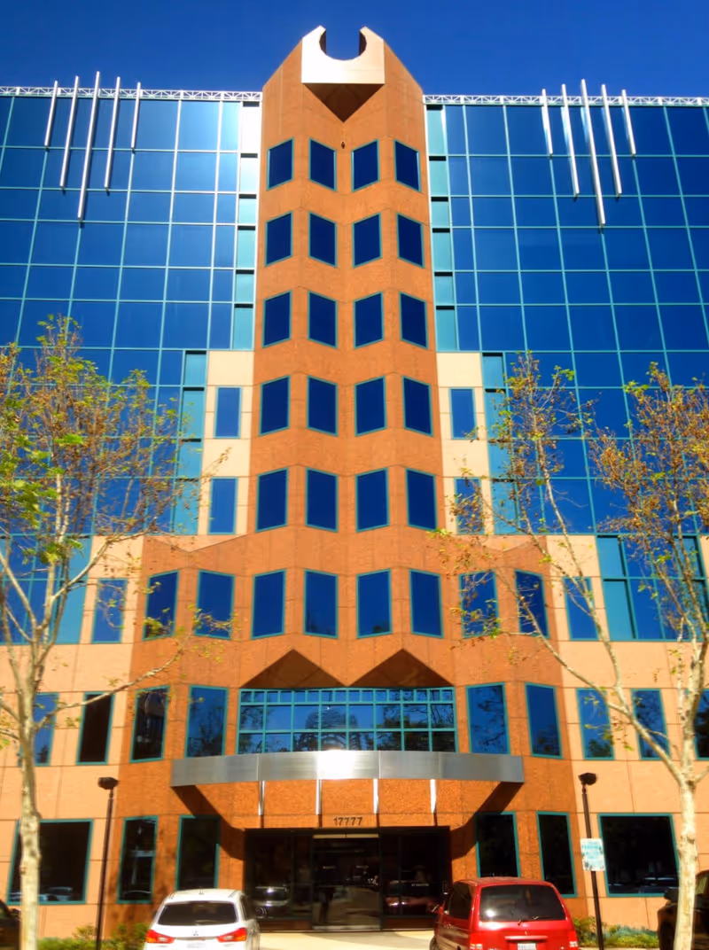 Sunlit glass-front building with brick central tower and main entrance.
