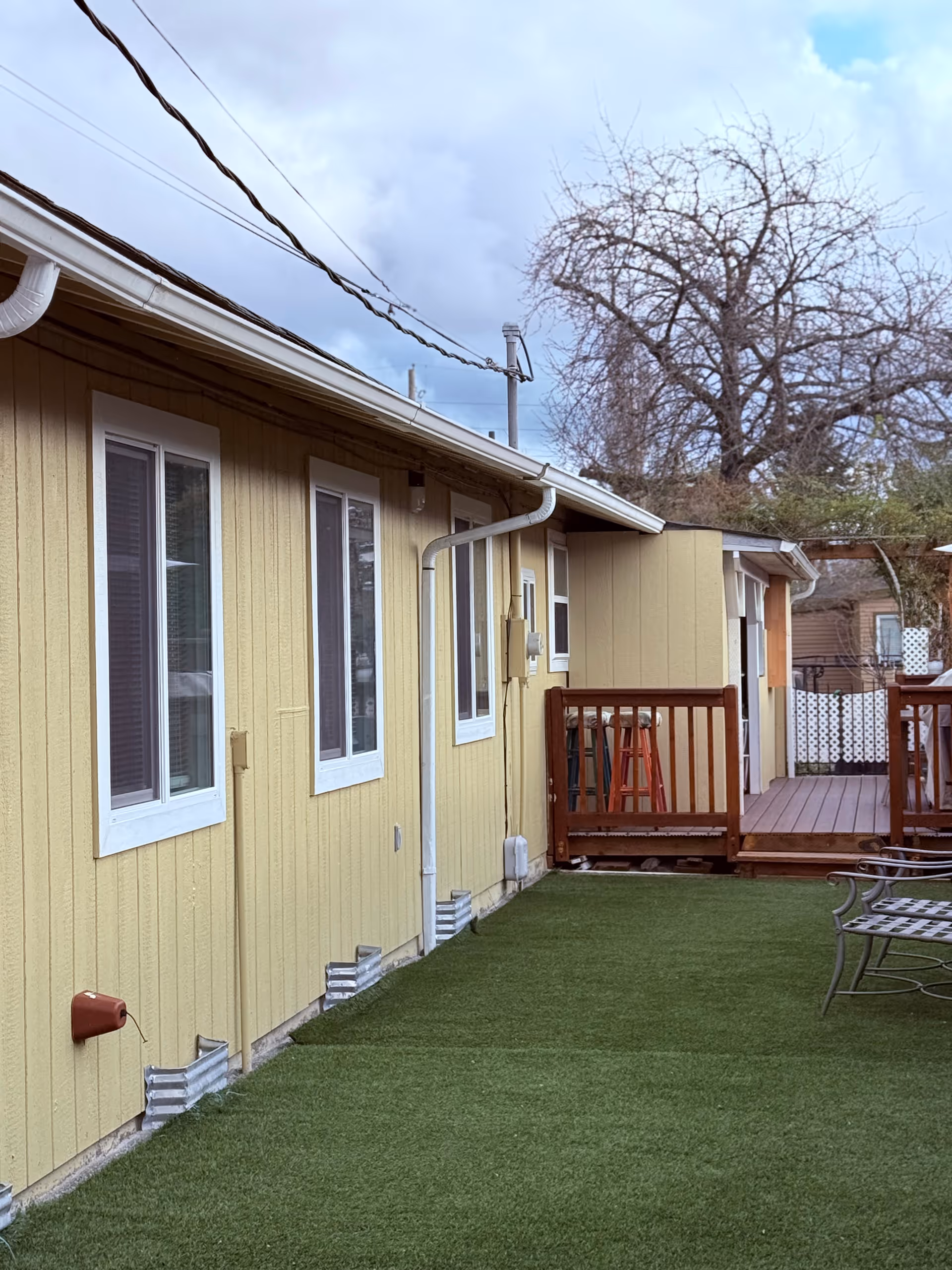 Exterior view of a yellow single-story senior home with a wooden deck and artificial turf.