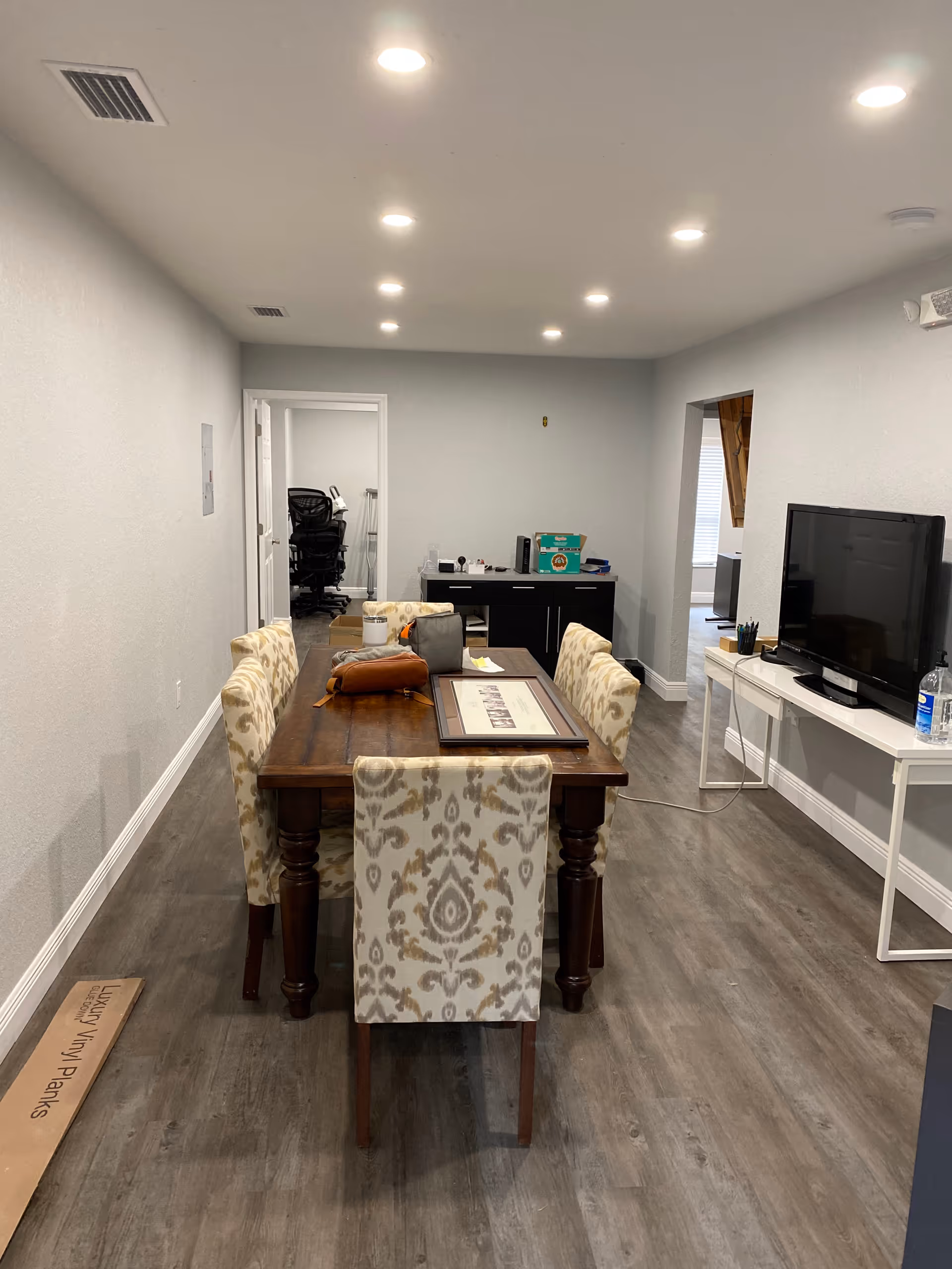 Dining room with a wooden table, six patterned chairs, and TV in a senior living facility.