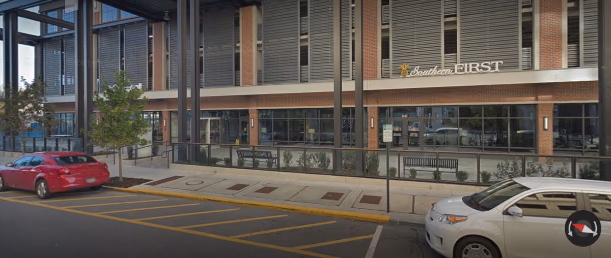 Exterior view of a brick building with glass storefront and parked cars along the street.