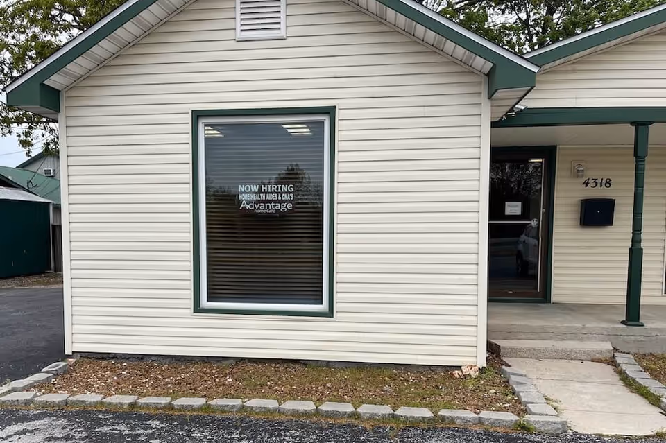 Exterior view of a beige building with a large window and a now hiring sign