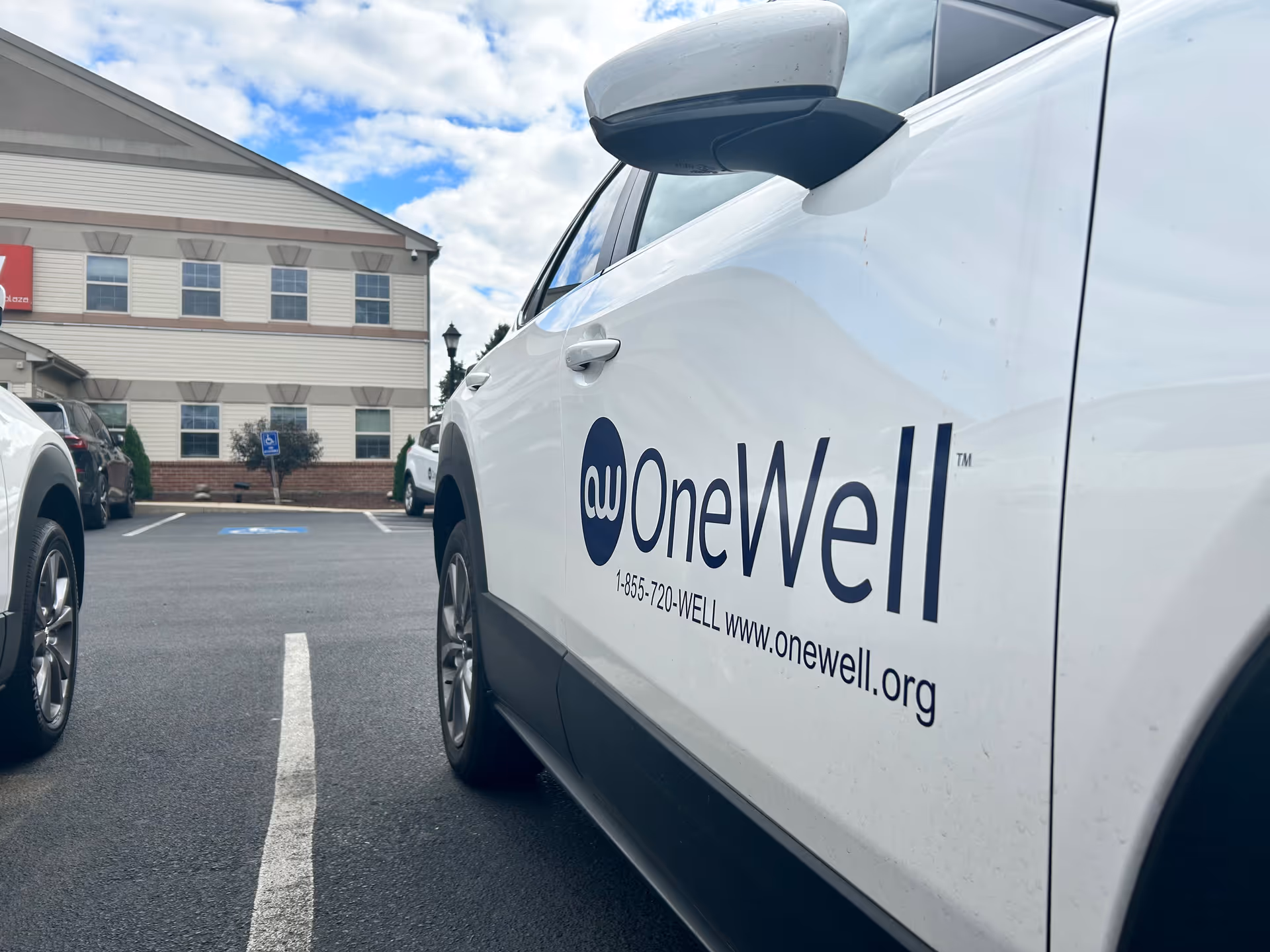 White van with OneWell branding parked in a lot near a beige facility.