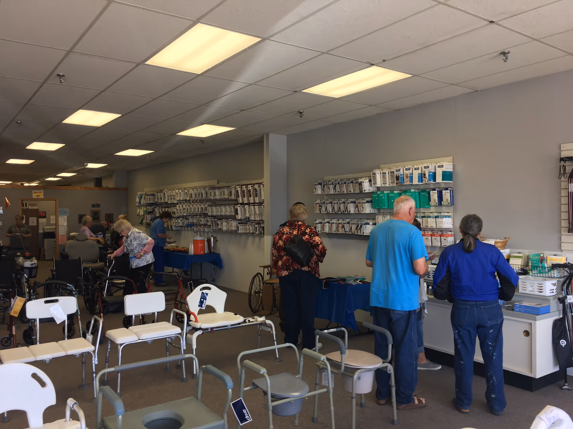 Interior of a senior facility with mobility aids, chairs, and people browsing.