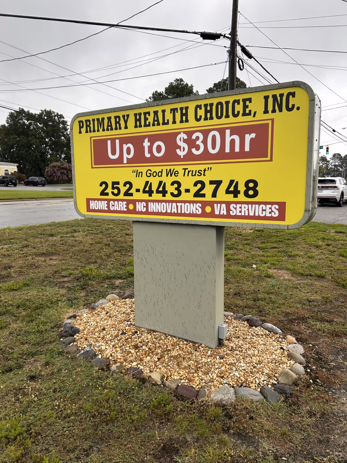 Bright yellow outdoor sign for Primary Health Choice on a gray pedestal in a parking lot.