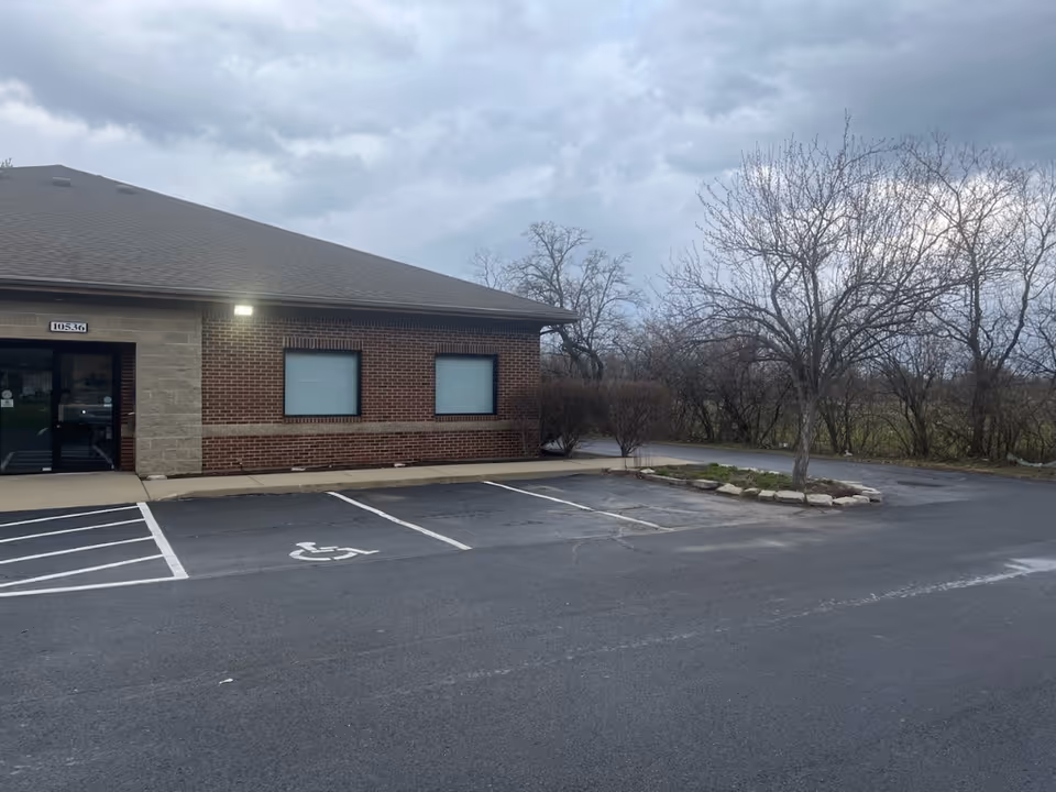 Brick senior care facility with a small parking lot and leafless trees beside the entrance.