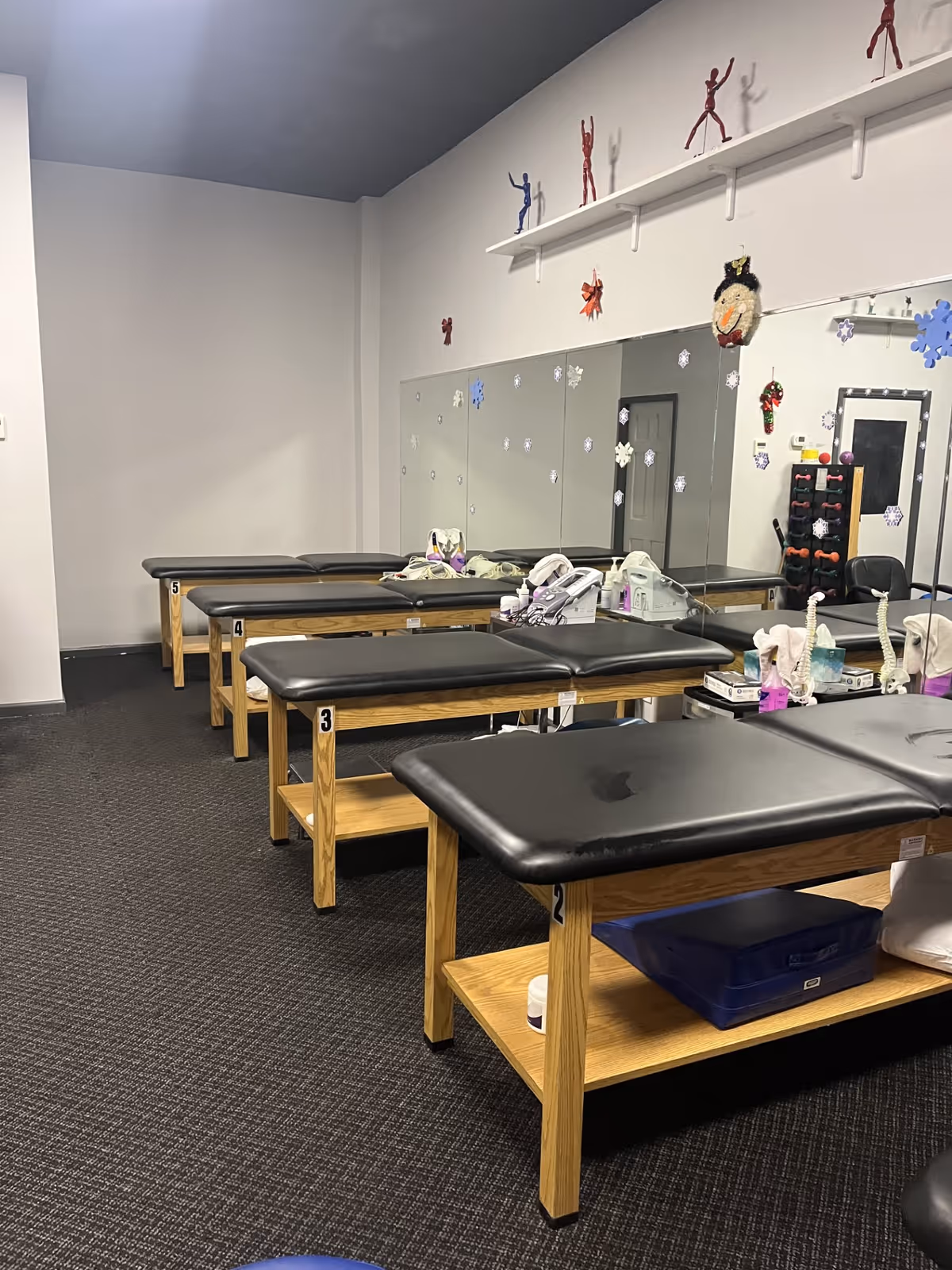 Clinic therapy room with several black-cushioned treatment tables, mirrors, and snowflake decorations