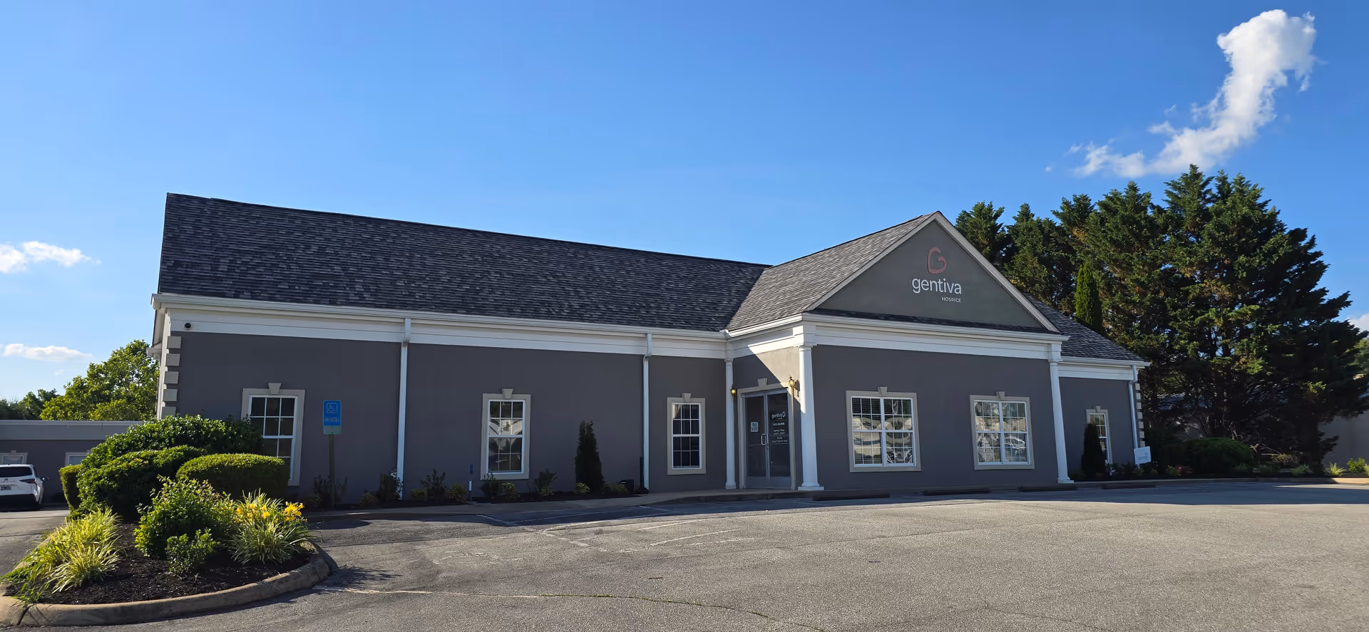 Front view of a Gentiva Hospice building with gray exterior, white columns, and a parking lot.