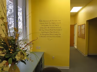 Bright yellow hallway with wall quote, windows, plants, and a counter near a reception area.