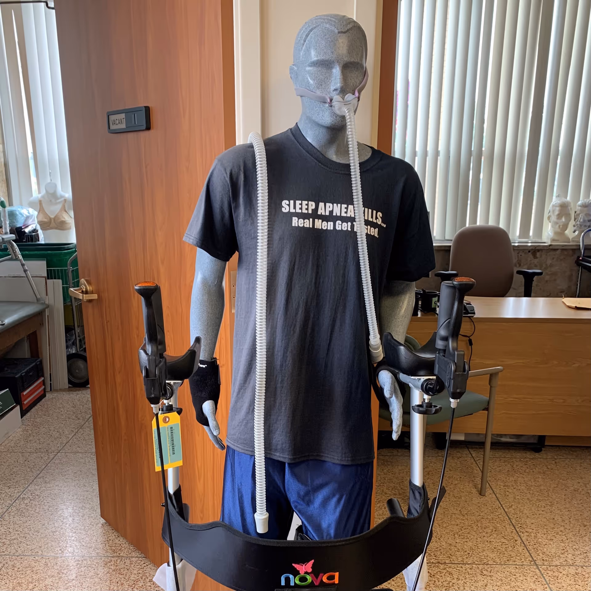 Life-size mannequin wearing a CPAP mask with tubing in a clinical office.