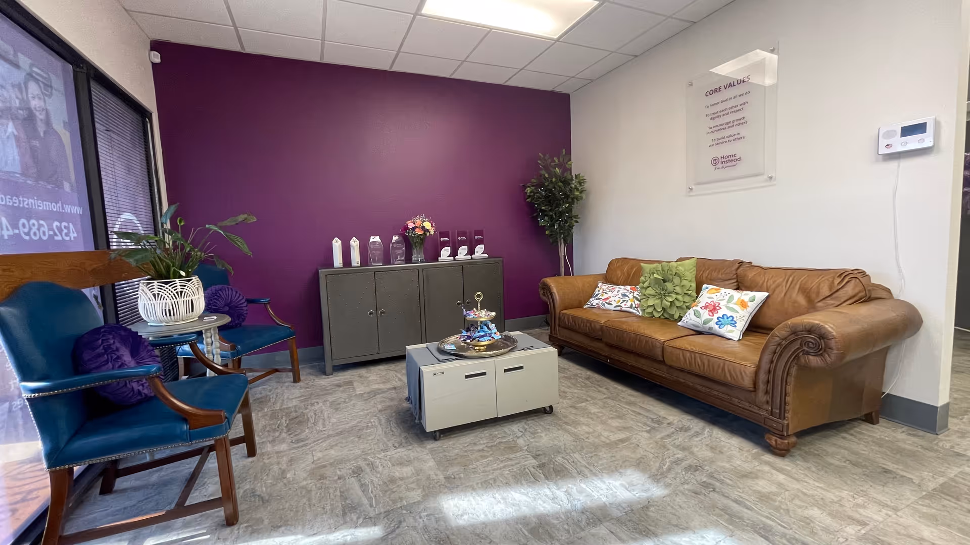 A cozy lounge area with purple accent wall, brown sofa, teal chairs, and a coffee table.