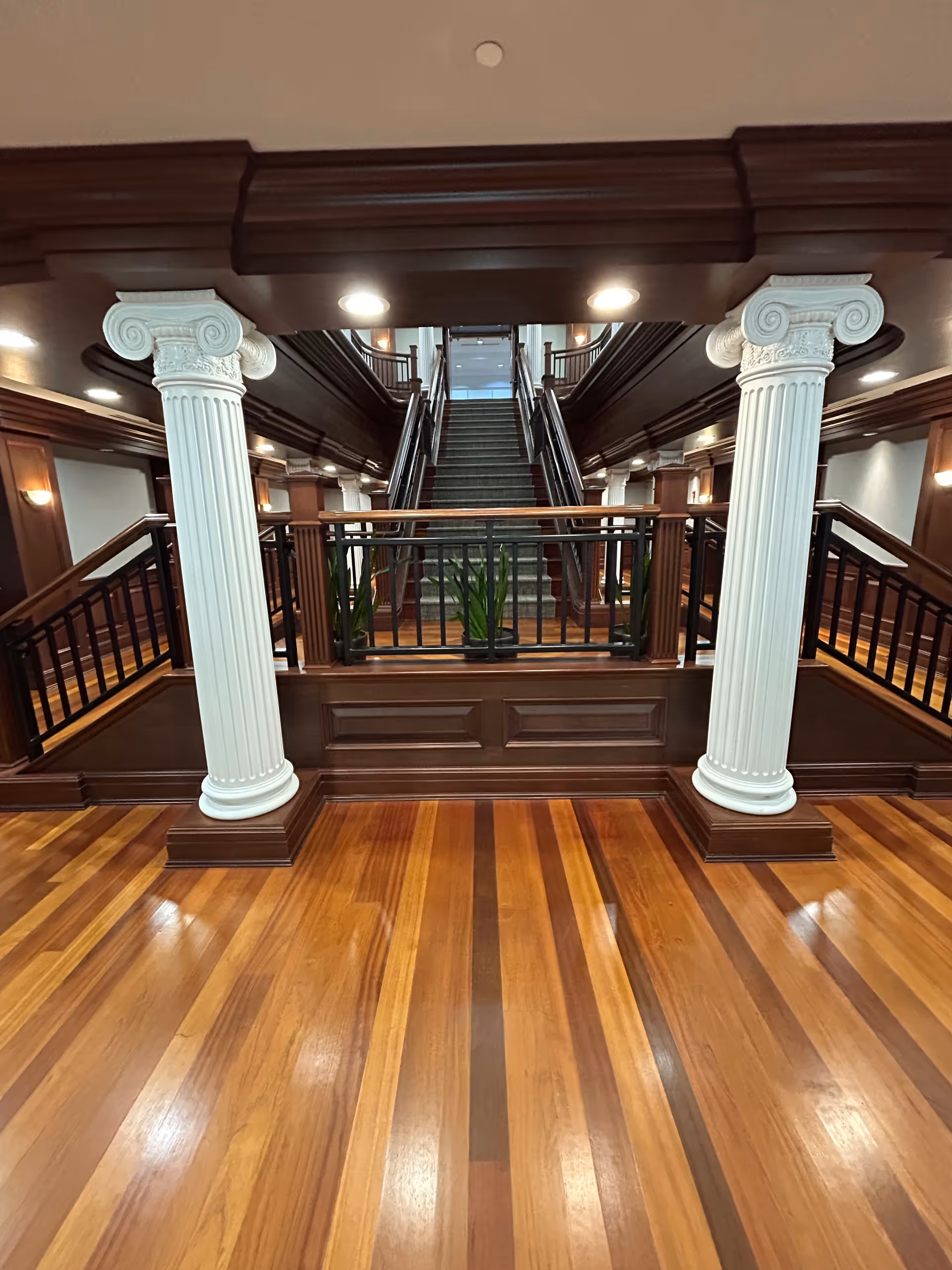 Interior atrium with white classical columns, dark wood railings, and a central staircase.