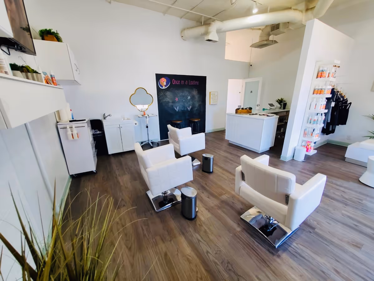 Modern salon interior with white chairs, styling stations, and a front desk.