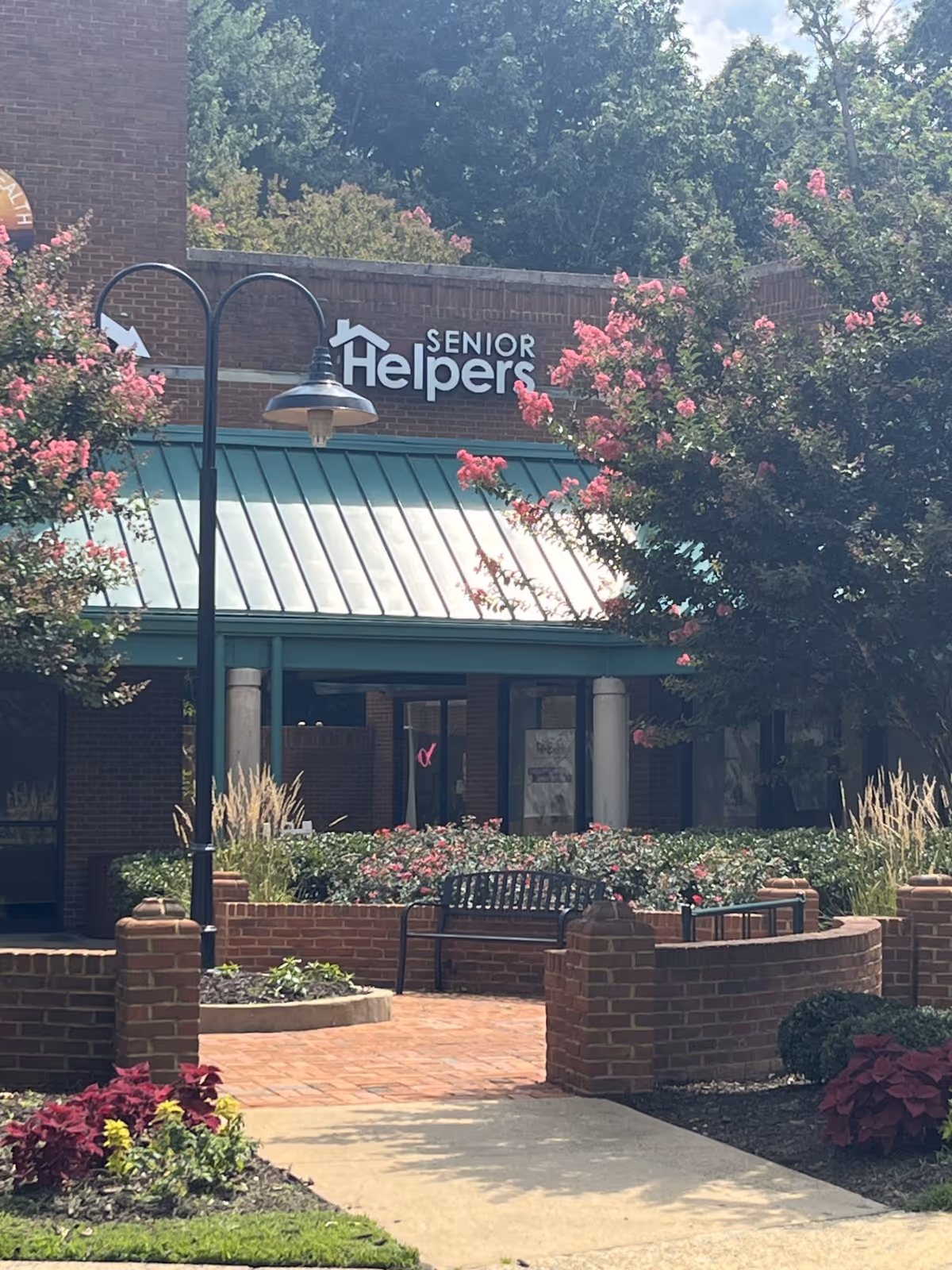Exterior view of a Senior Helpers facility entrance with brick walls, benches, and landscaping.
