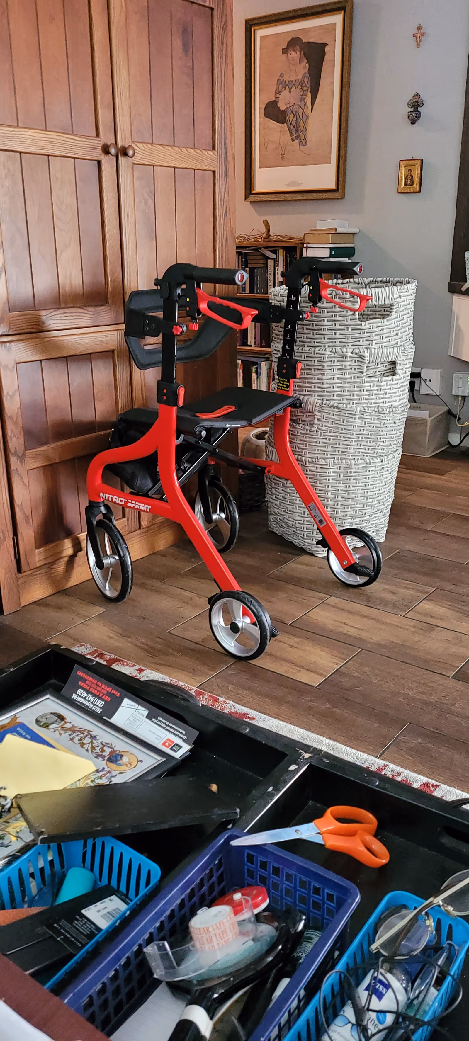 Red walker in a cozy senior living room with wooden cabinets, wicker basket, and scattered supplies.