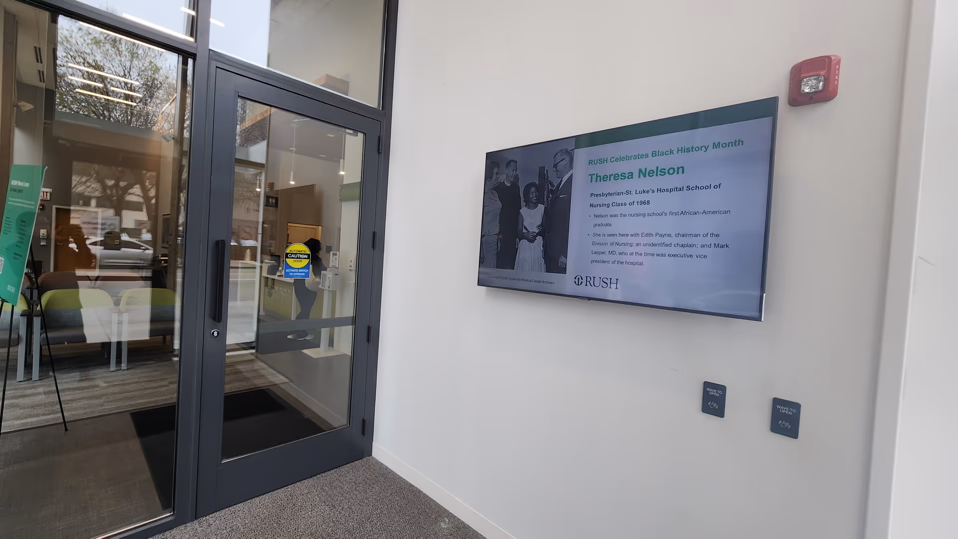 Lobby entrance of Rush West Loop with glass doors and a wall-mounted information screen.