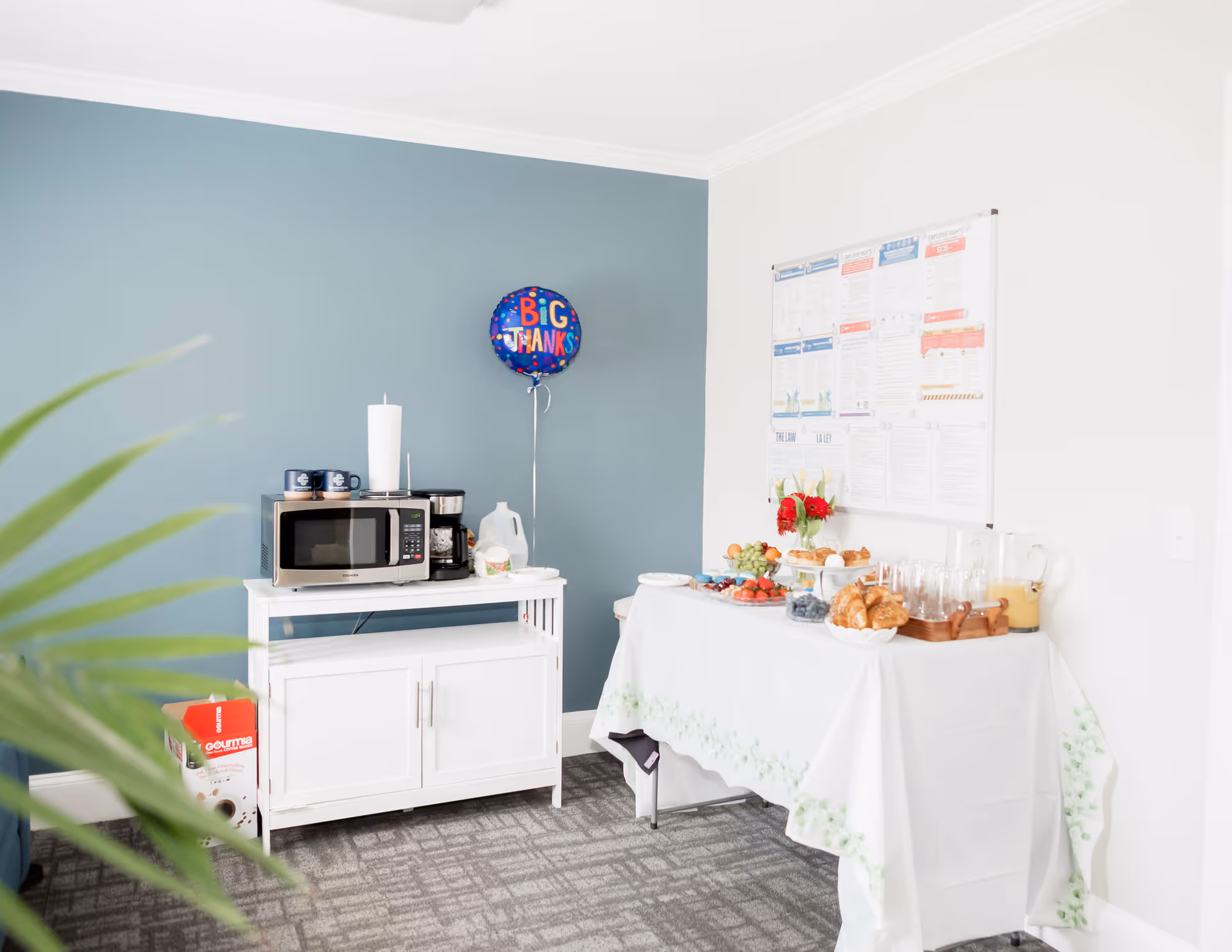 Small interior break area with microwave, snack table, balloon, and blue accent wall.