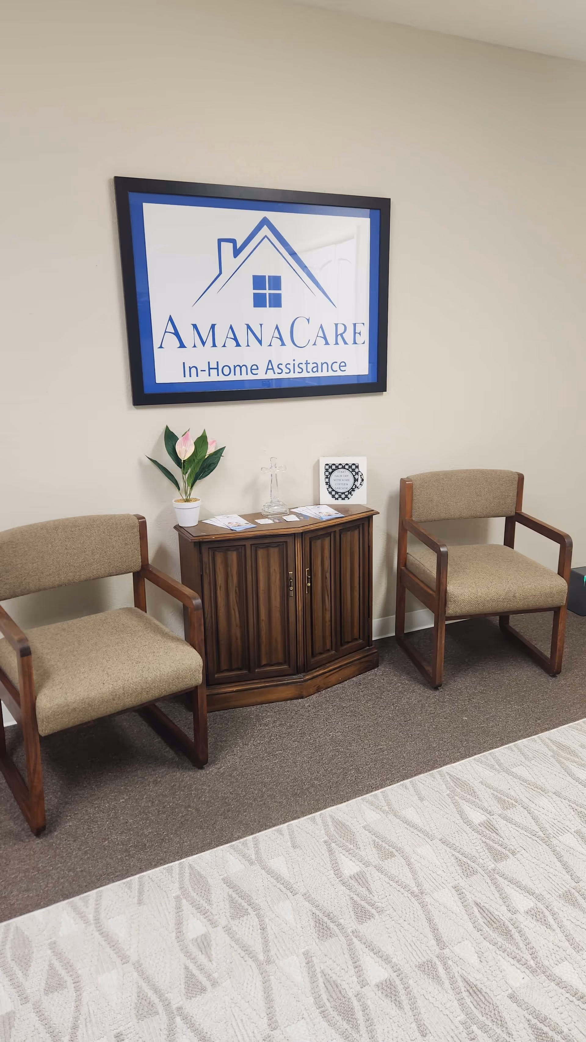 Interior waiting area with two beige chairs, a wooden cabinet, plant, and AmanaCare sign.