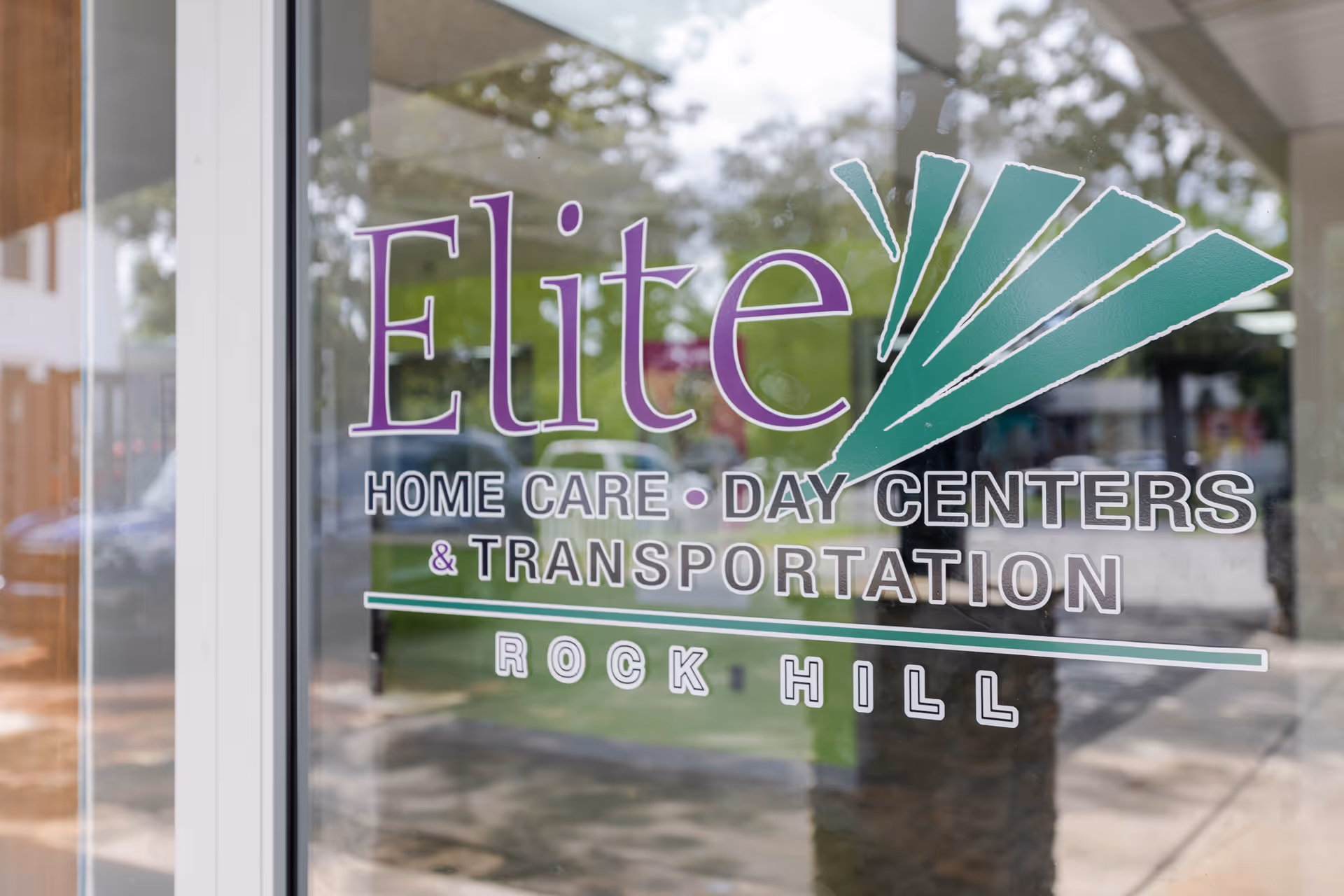 Window signage reads Elite Home Care Day Centers & Transportation, Rock Hill, reflected outdoors.