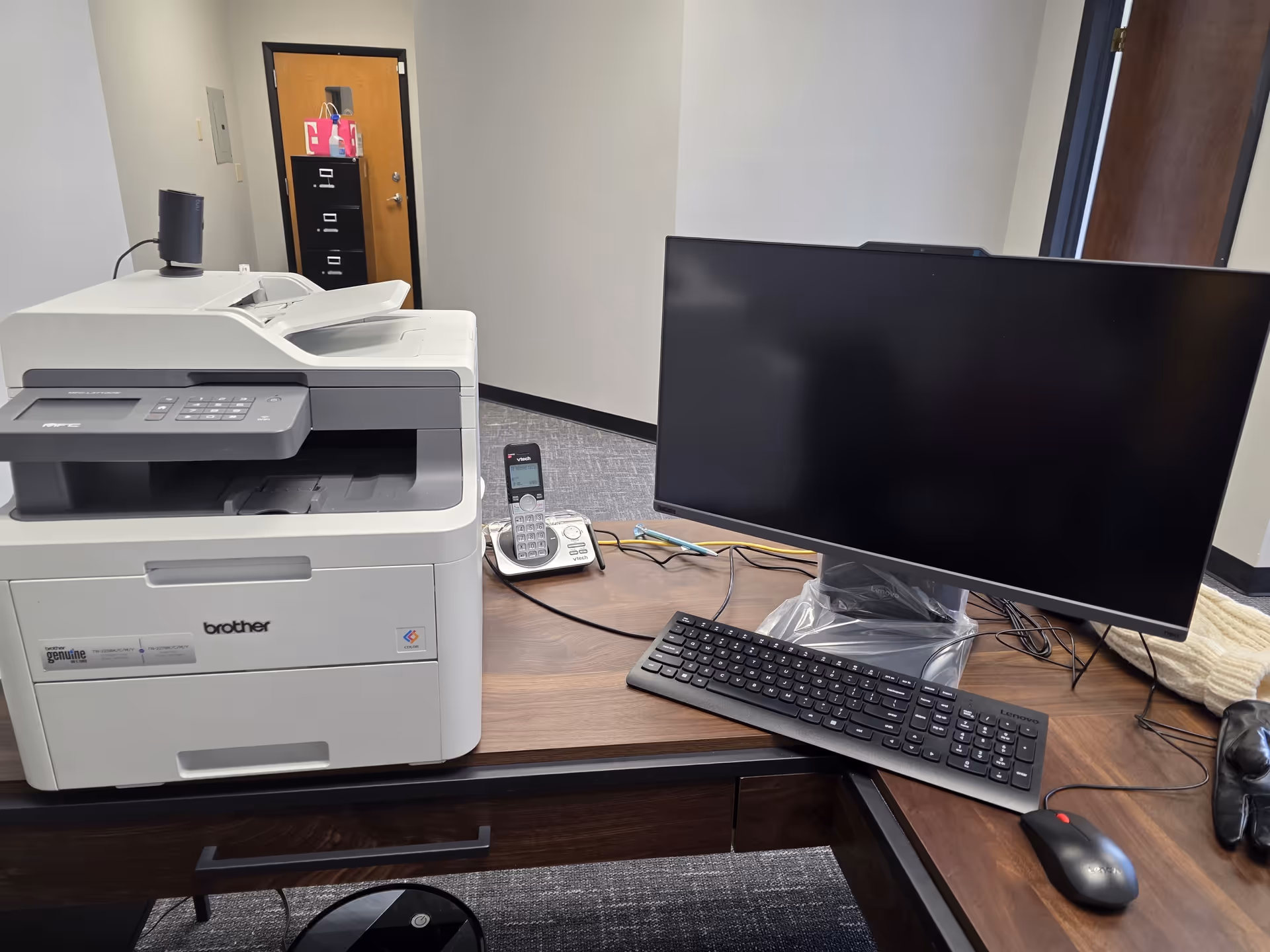 Interior office desk with printer, monitor, keyboard, and phone on a dark desk.