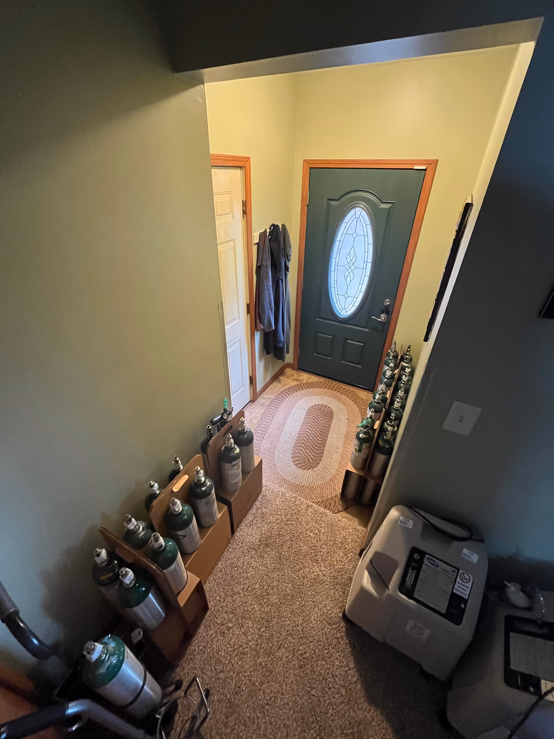 Narrow interior entry hall with a green front door, coats, and stacked oxygen tanks along walls.