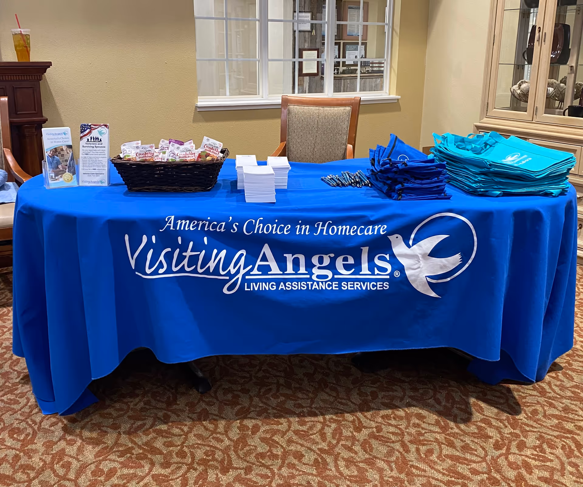 Indoor reception table with a blue Visiting Angels banner and brochures.