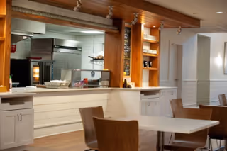 Open dining area with white counter, stools, and wooden cabinets in a senior living facility.