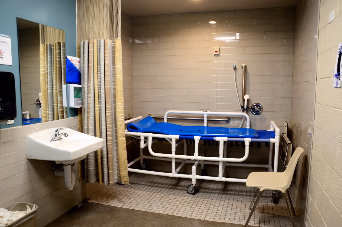 Clinical bathroom area with a blue patient stretcher, sink, and curtain.