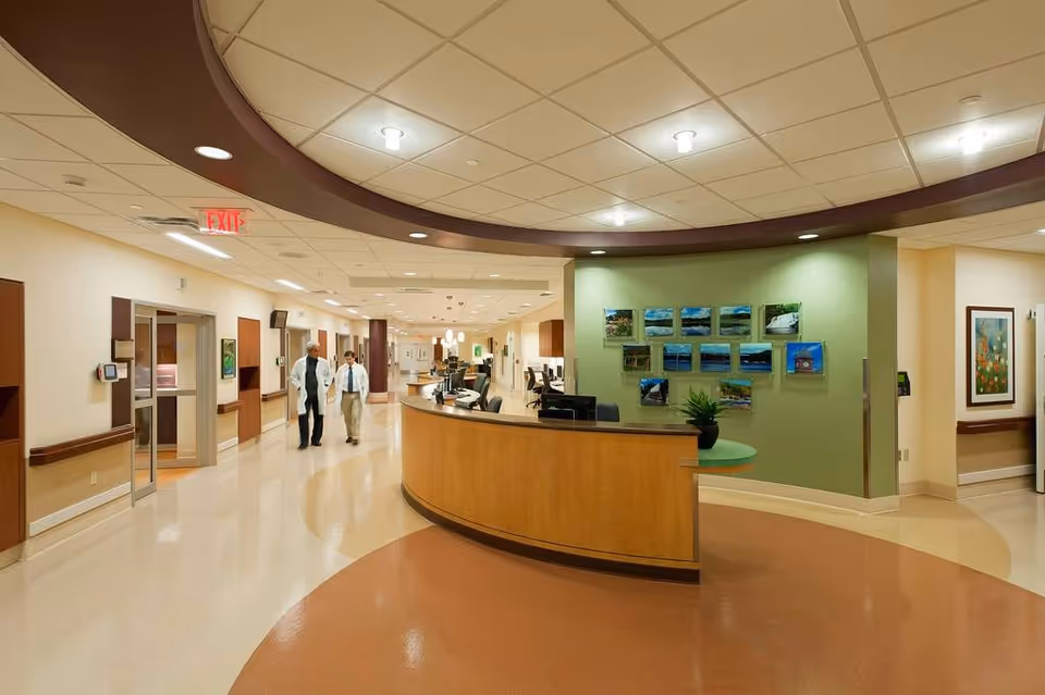 A hospital lobby with a curved front desk, green wall art, and two staff walking.