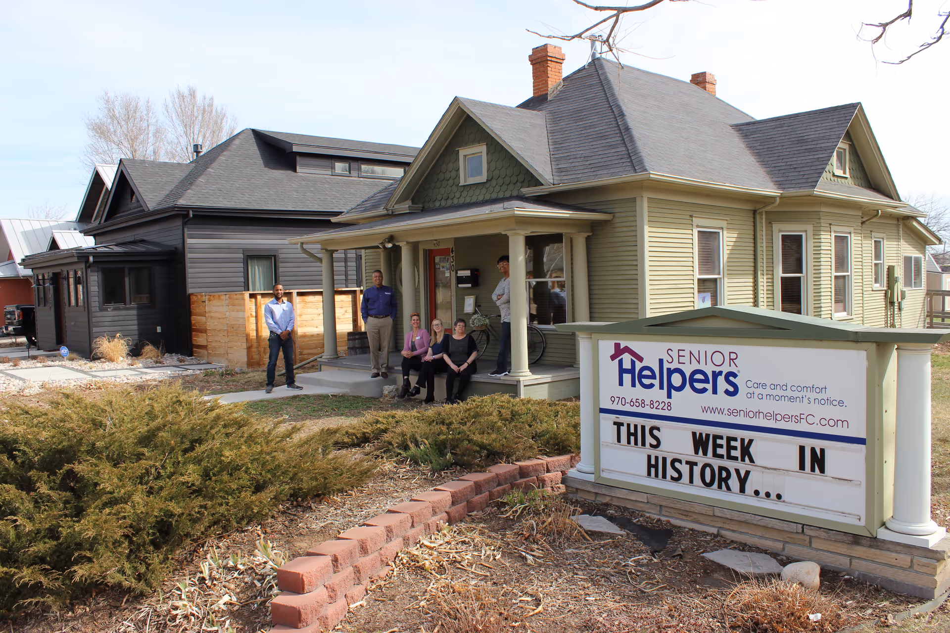Exterior view of Senior Helpers facility with a sign and several people on the front porch.