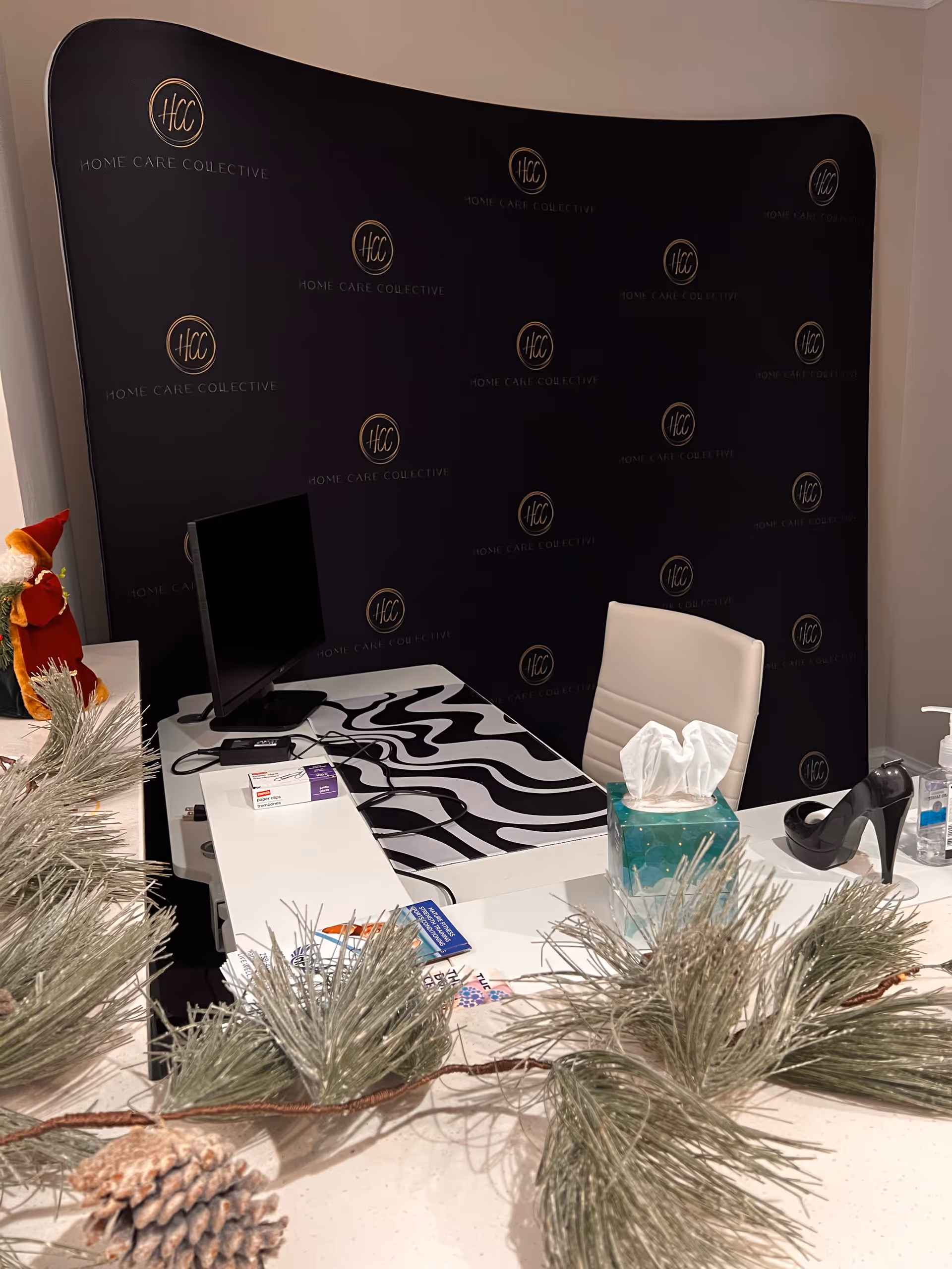 Reception desk inside Home Care Collective with branded backdrop, computer, tissue box, and pine decor.