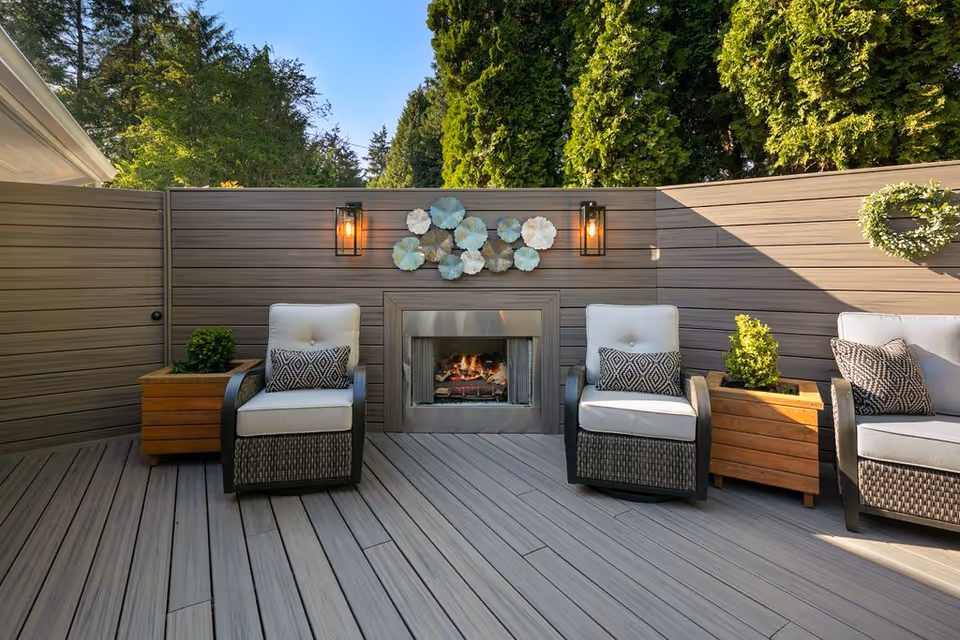 Outdoor deck with wicker seating, a central fireplace, potted plants, and decorative wall art.