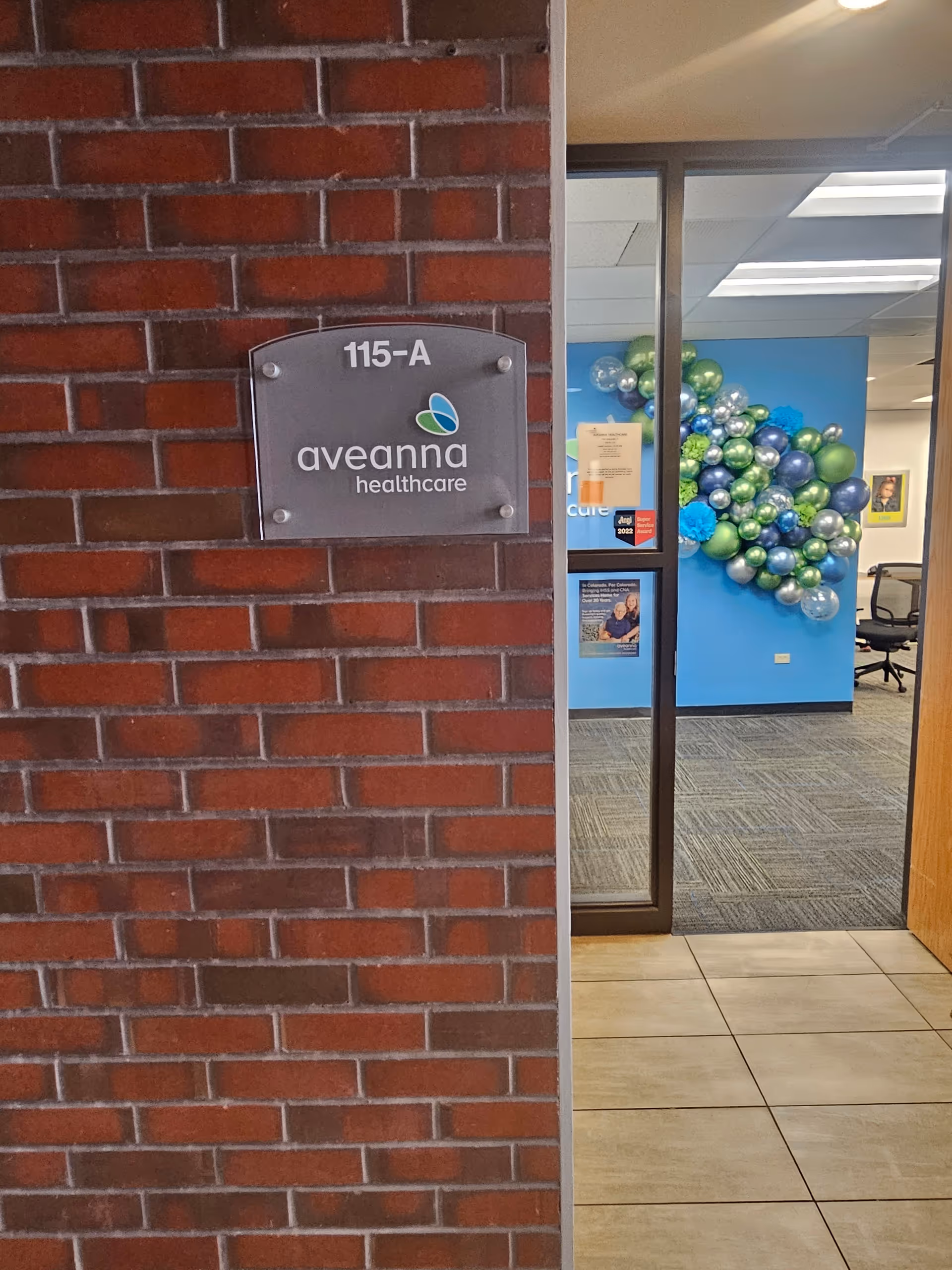 Brick wall plaque reading Aveanna Healthcare beside glass door to a decorated reception area.