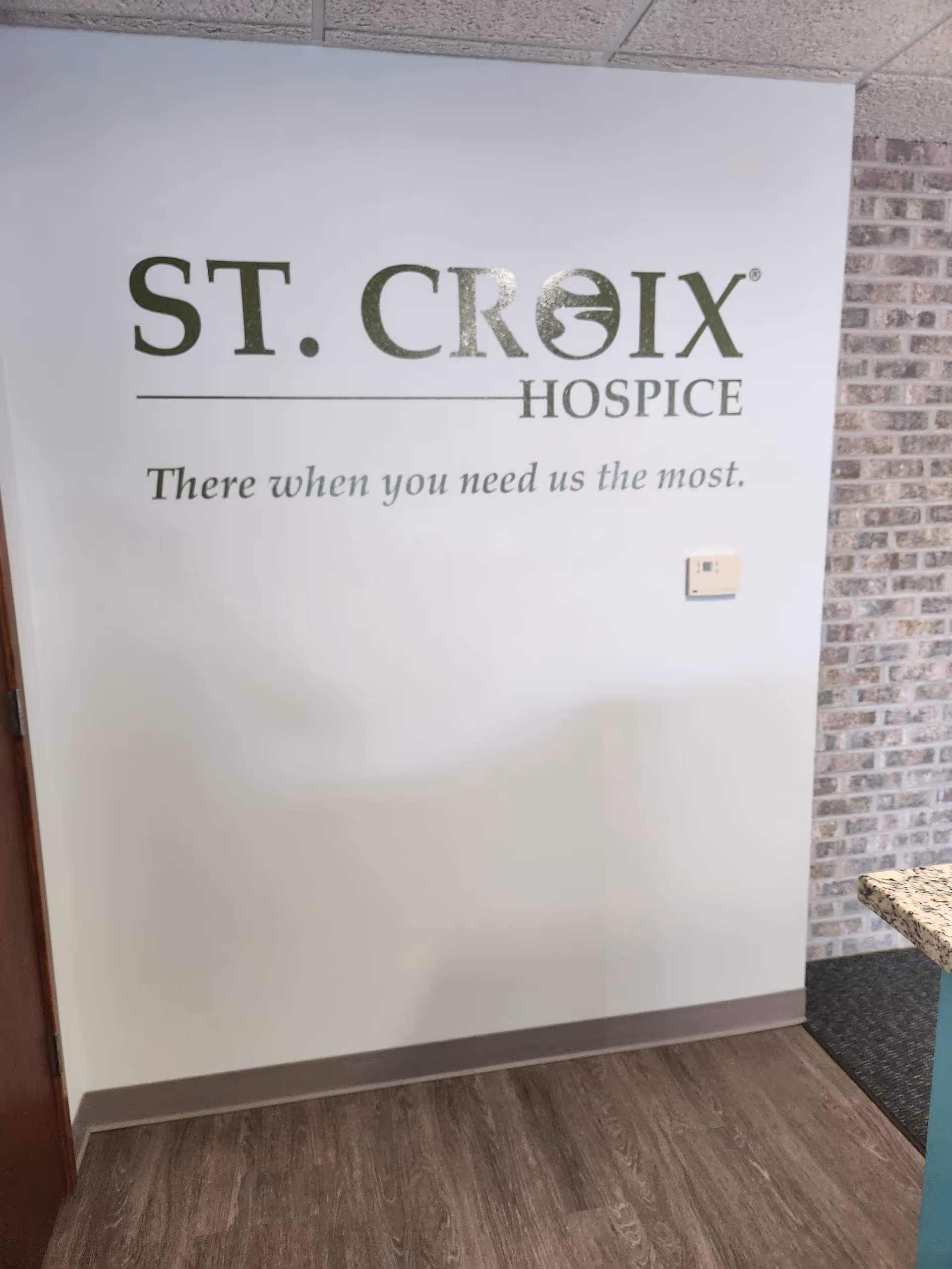 Indoor wall signage reads St. Croix Hospice with slogan and brick accent wall nearby.