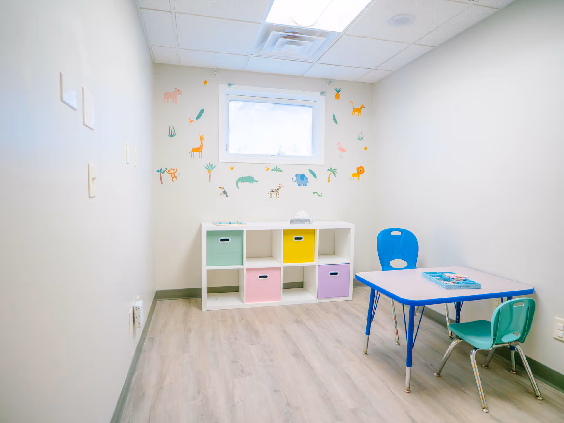 Bright playroom with a small table, colorful chairs, and cubby storage.